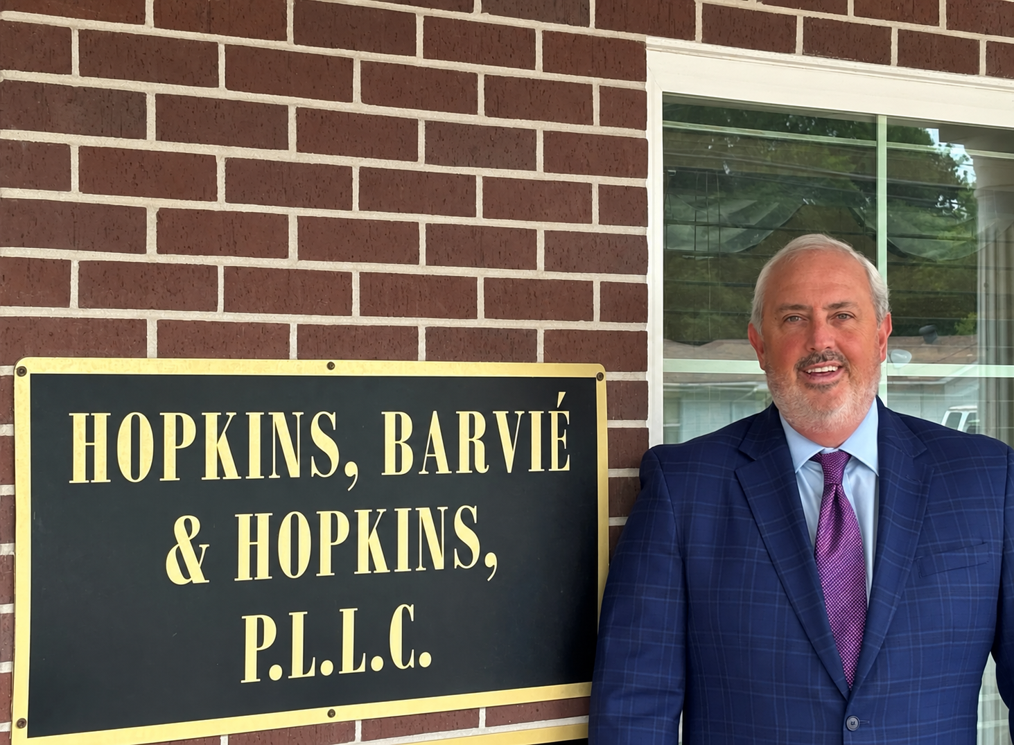 Law office sign reading “HOPKINS, BARVIE & HOPKINS, P.L.L.C.” beside a man in a suit