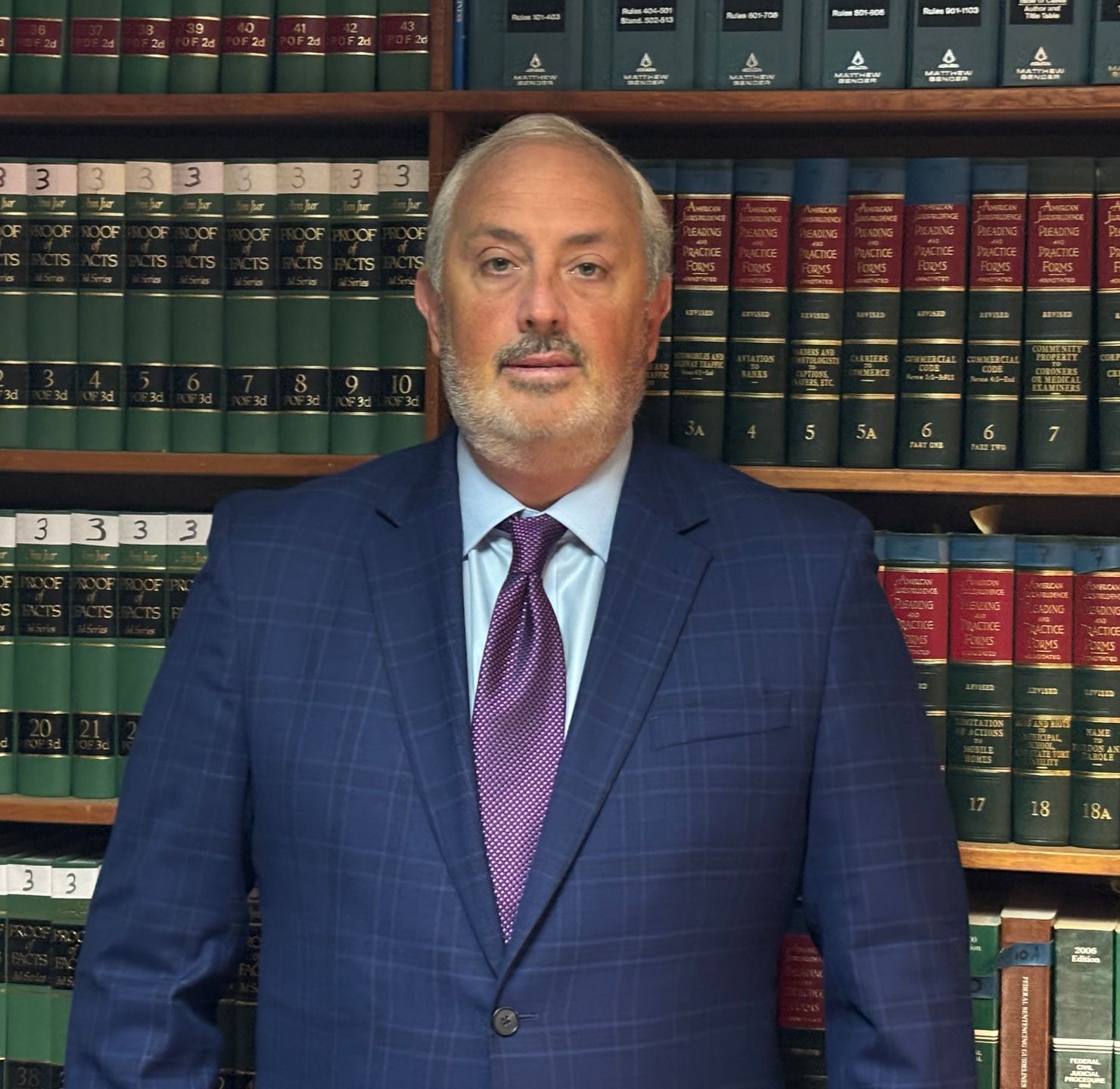 Man in a blue suit and purple tie stands before shelves of law books.