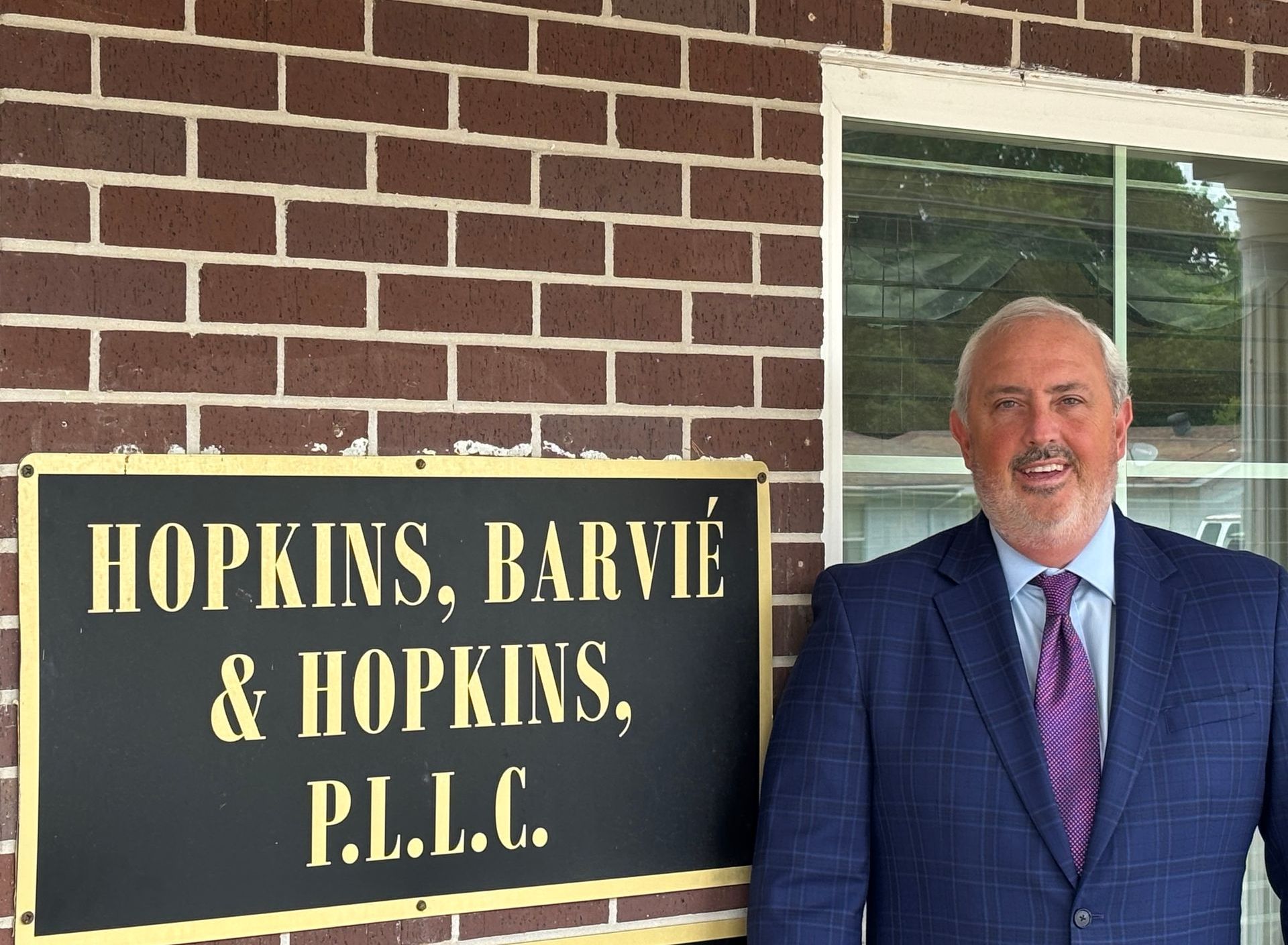 Law office sign reading “HOPKINS, BARVIE & HOPKINS, P.L.L.C.” beside a man in a suit