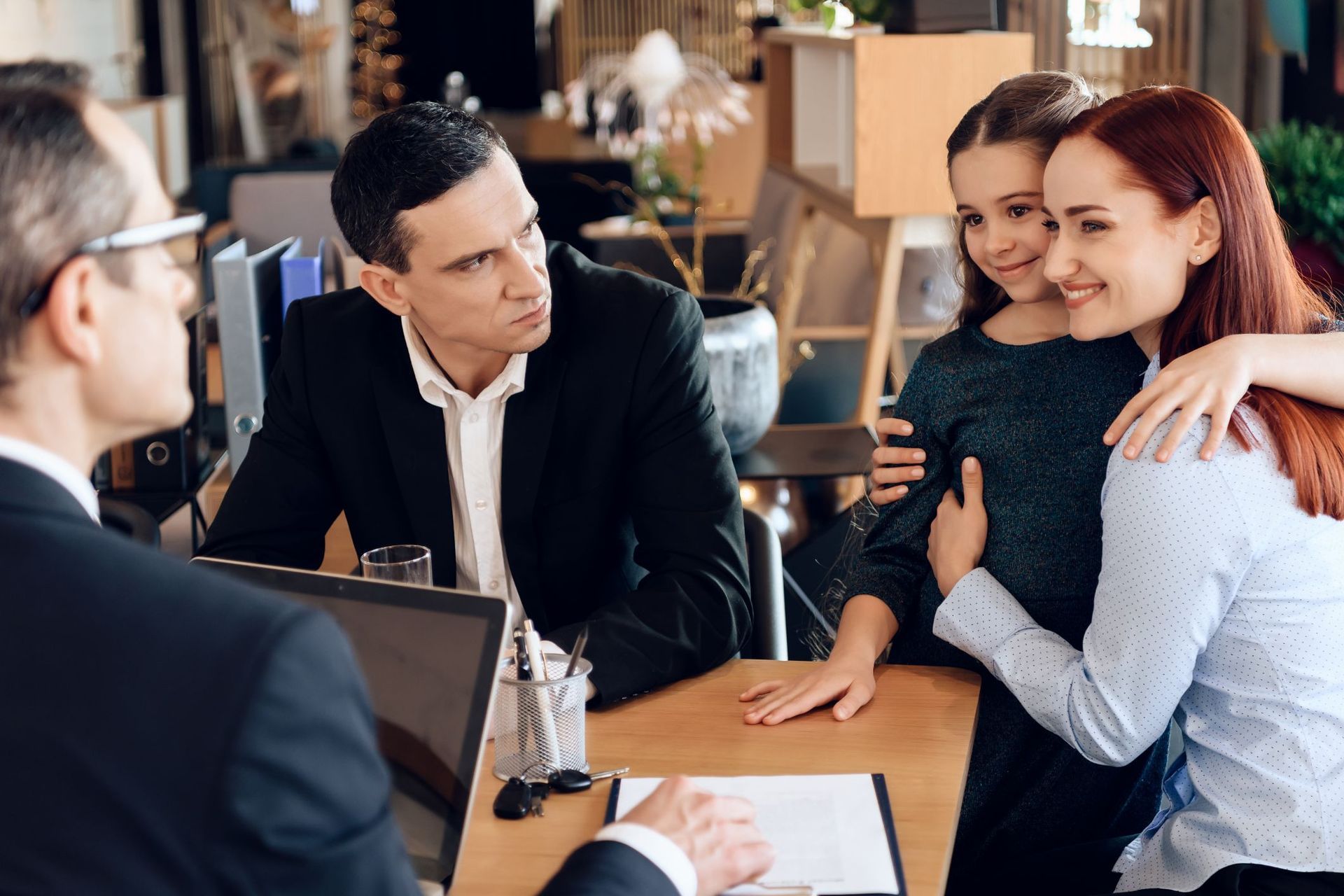 Three people smile and hug in a business meeting at a table with papers and a laptop.