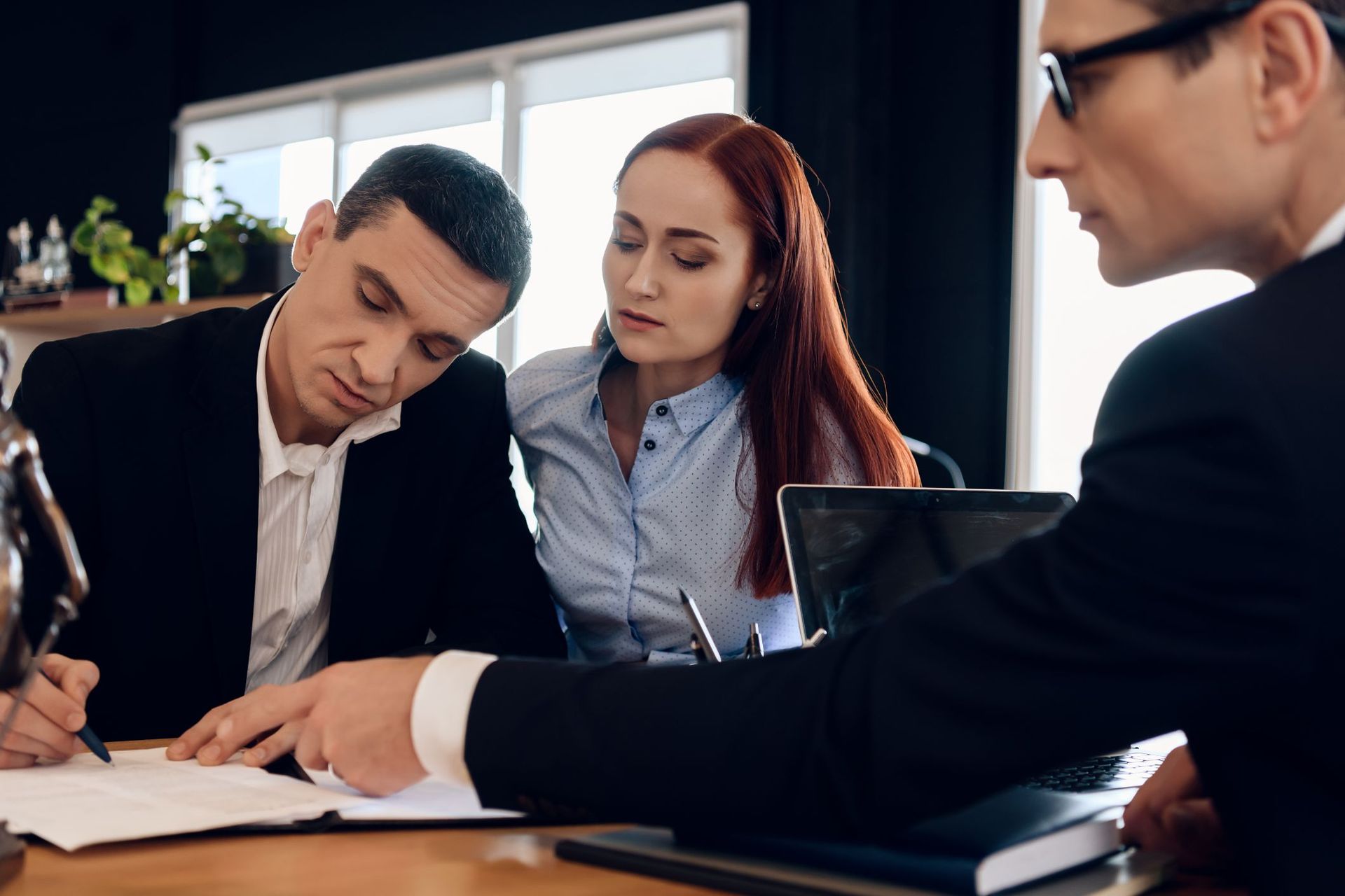 Three coworkers in a meeting, reviewing documents at a table in a bright office.