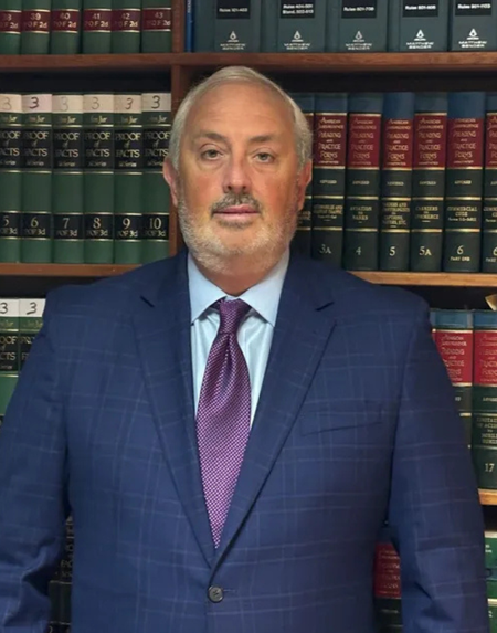 Man in a blue suit and purple tie standing before law books in a library or office setting