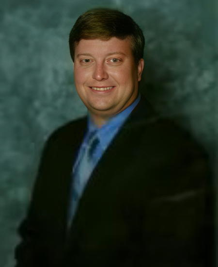 Studio portrait of a smiling man in a dark suit and blue shirt against a green background