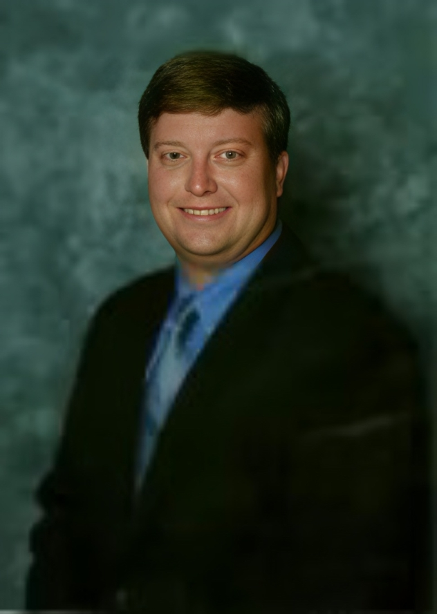 Studio portrait of a man in a dark suit and blue shirt against a mottled green backdrop