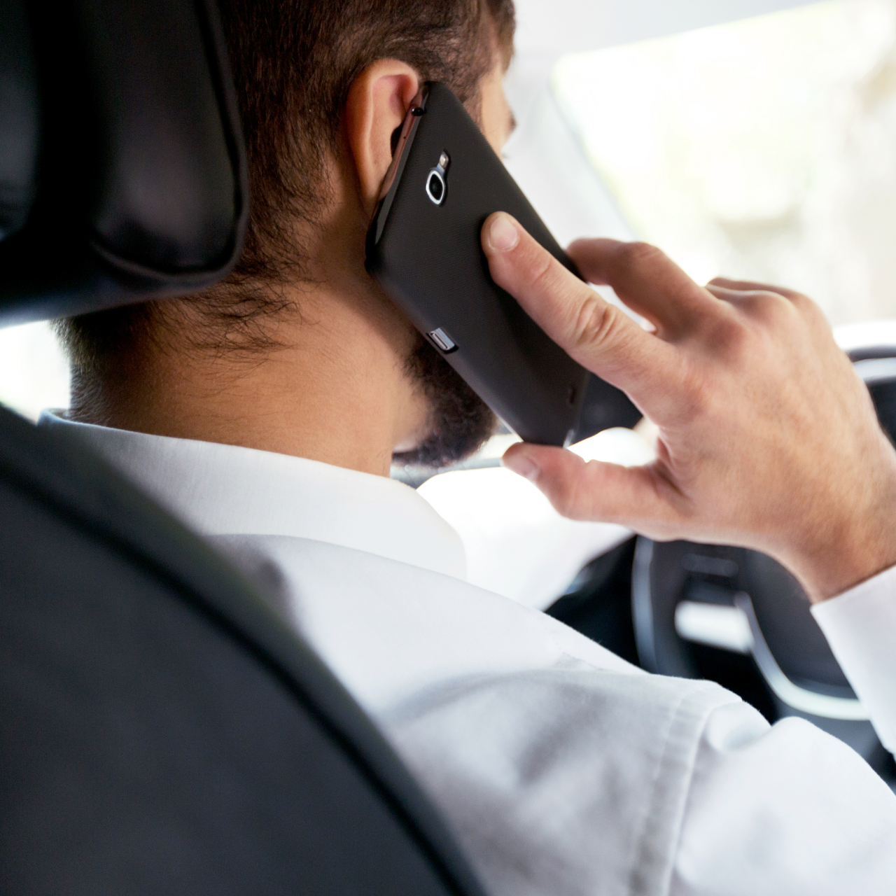 Person in a suit talking on a smartphone in the back seat of a car