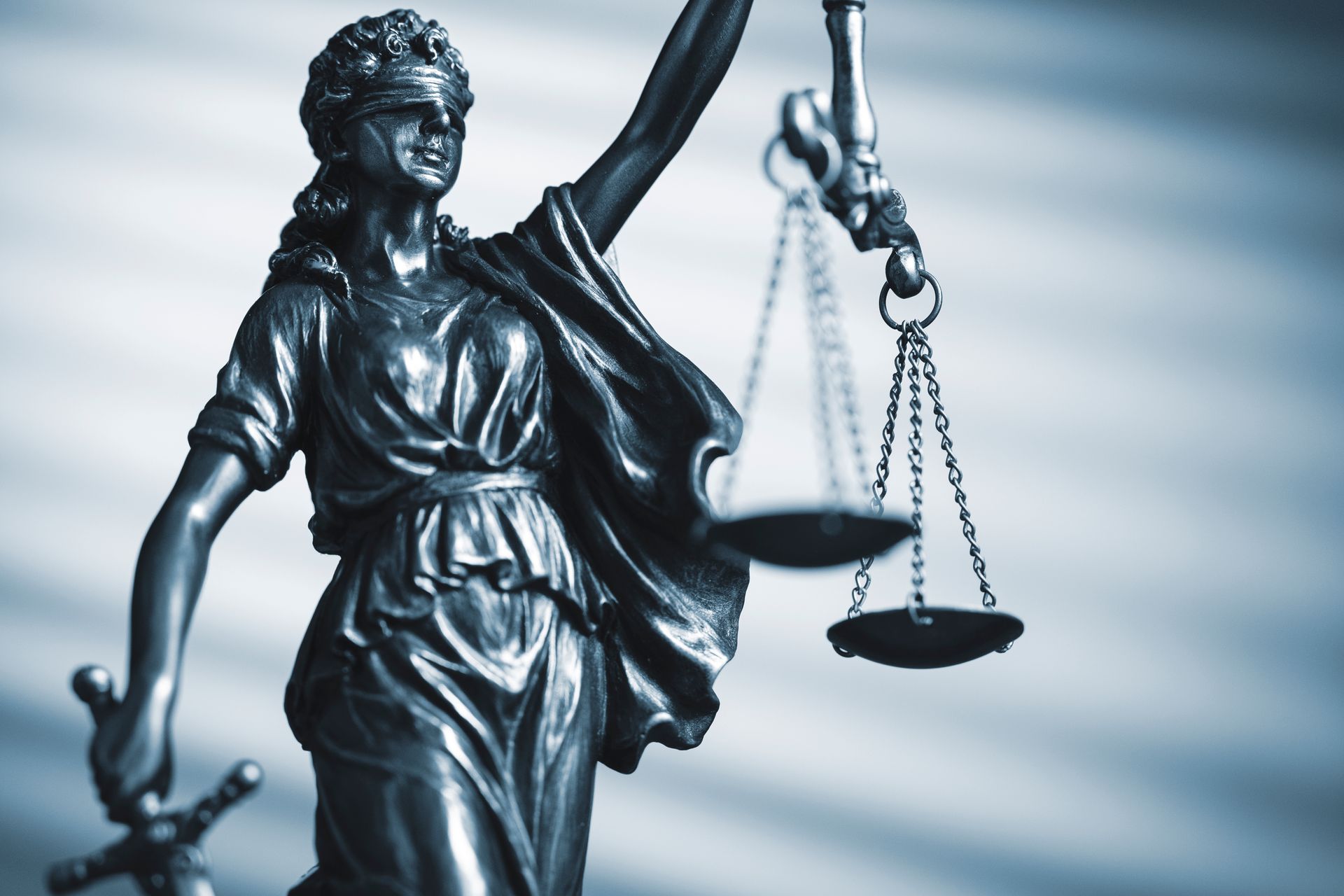 Bronze Lady Justice statue holding scales with a blue-gray background