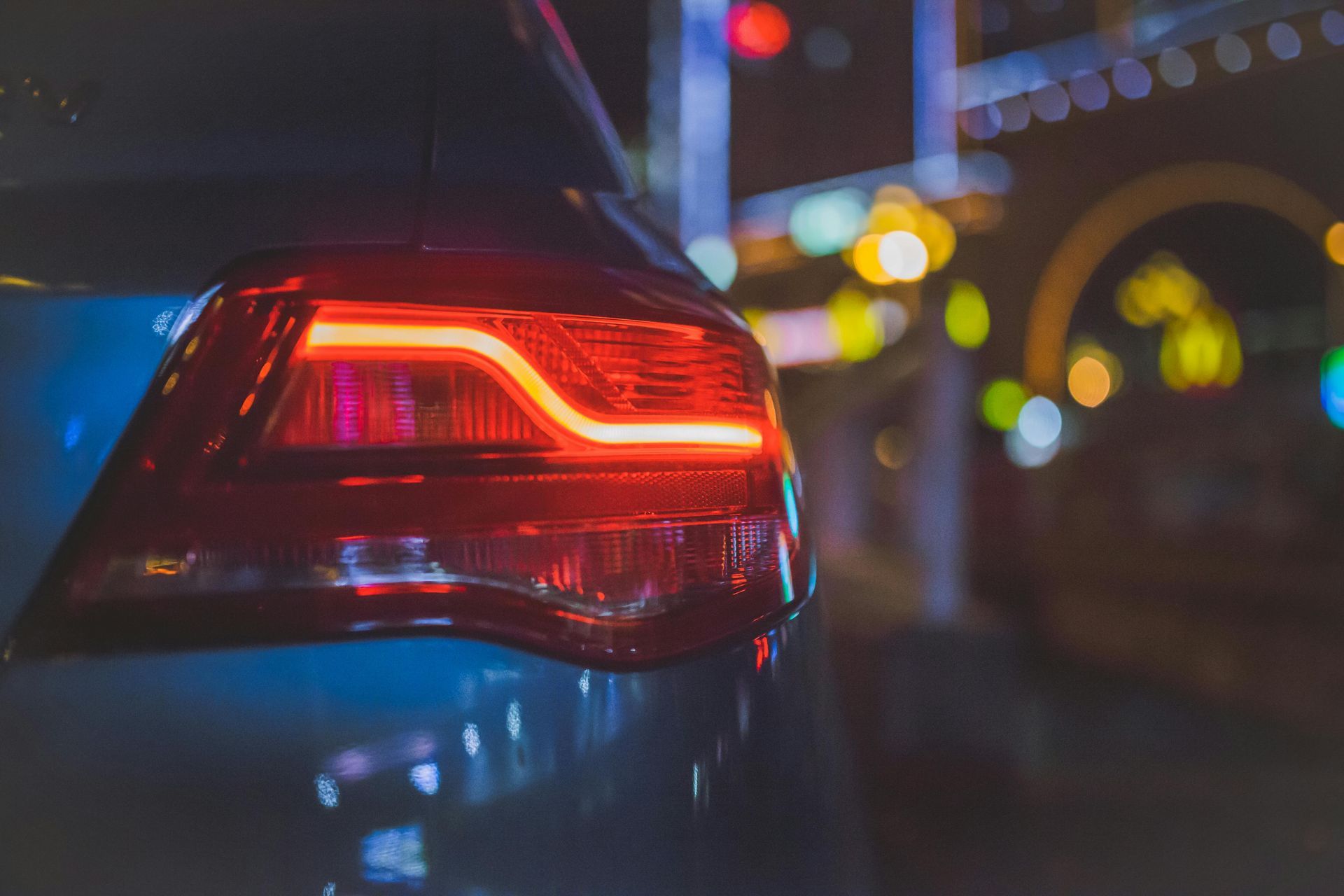 Rear view of a blue car at night with glowing red taillight near blurred streetlights
