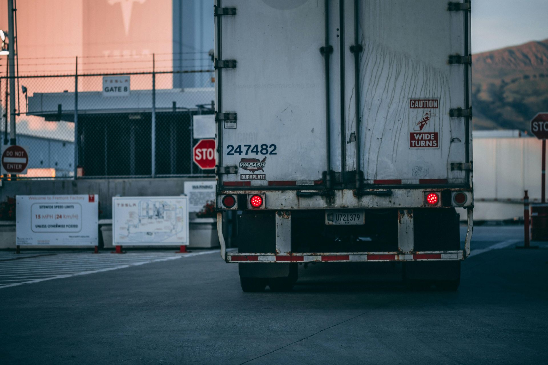 Rear view of a white cargo truck at a checkpoint near an industrial building at dusk