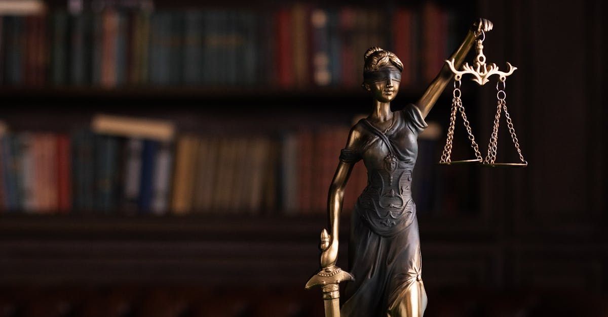 Bronze Lady Justice statue holding scales and a sword, with blurred law books in the background