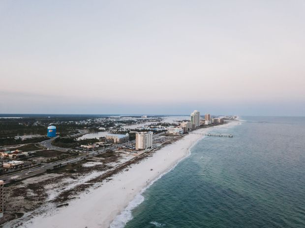 Aerial view of a white sandy beach and coastal buildings beside calm blue water at sunset