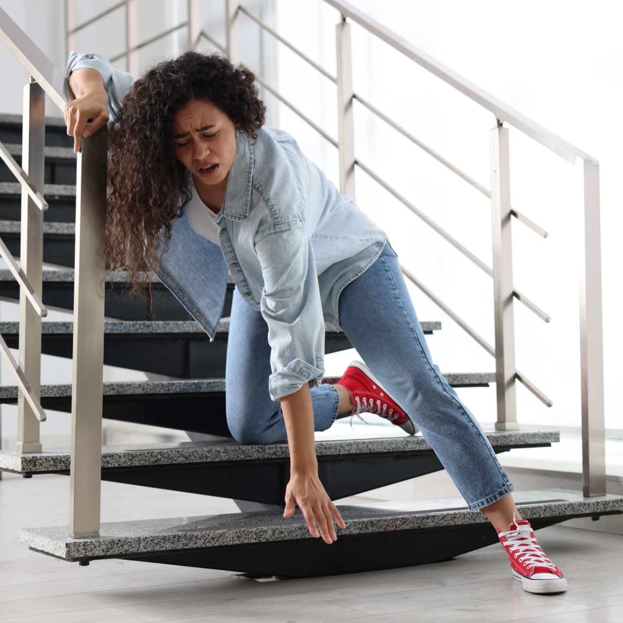 Woman in denim jacket slipping on outdoor stairs, bracing herself on the railing.