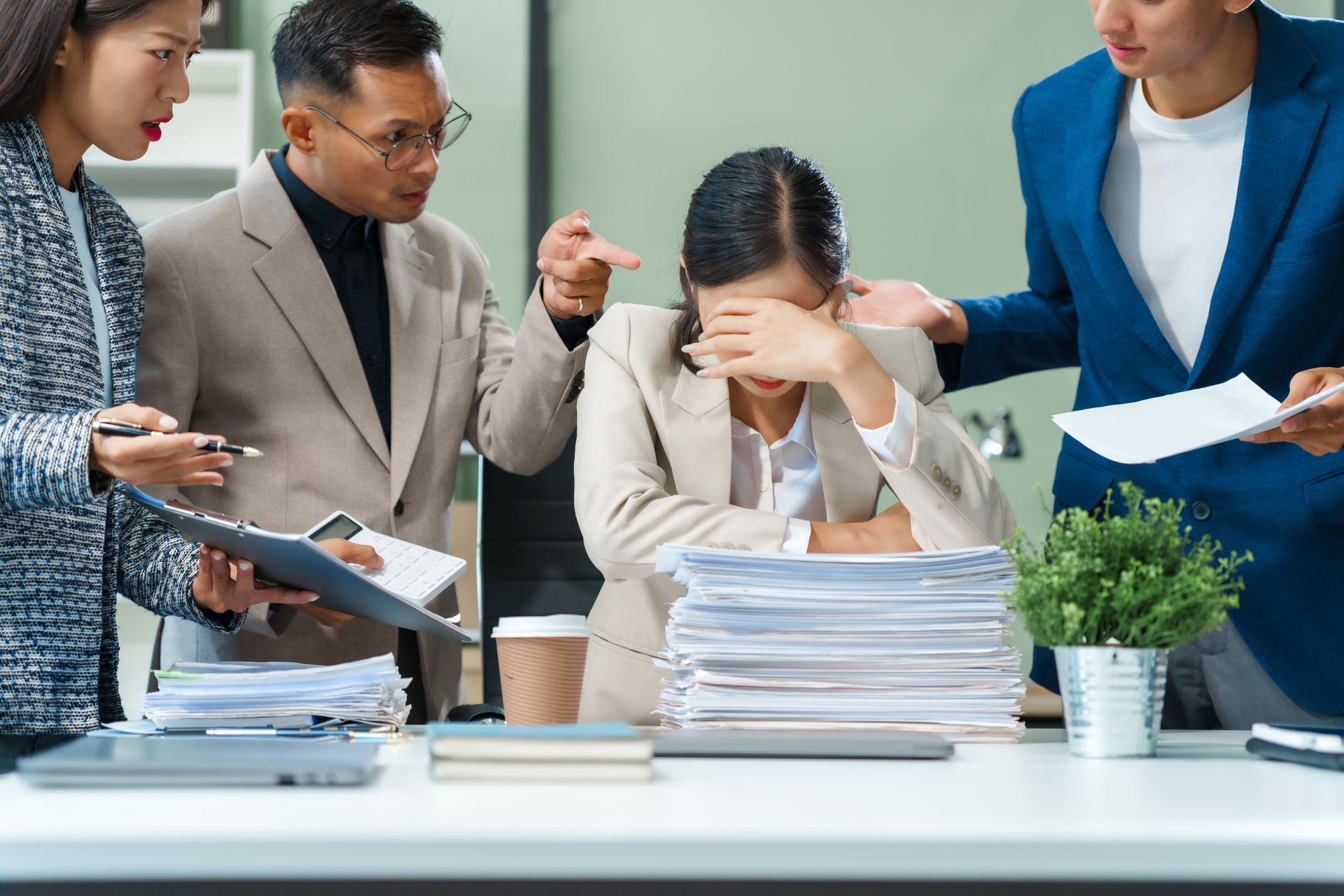Office team discussing over documents, with one person stressed and covering their face at a desk