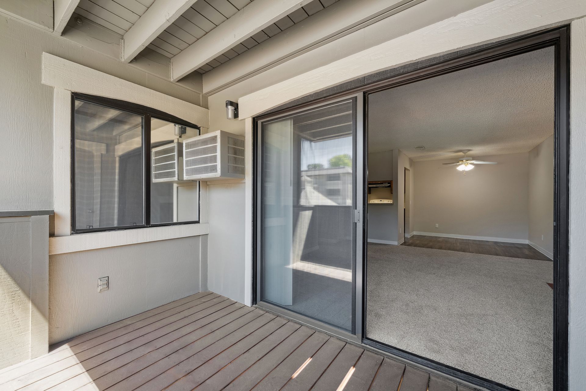 Covered patio with sliding glass door, window AC unit, and view into a carpeted room