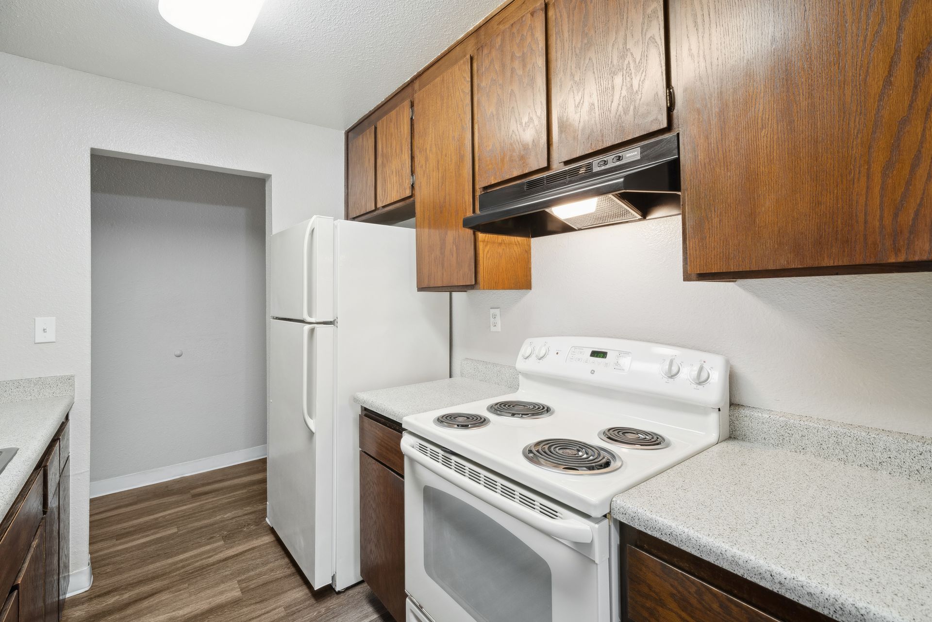 Kitchen with white appliances, wood cabinets, and speckled countertops.
