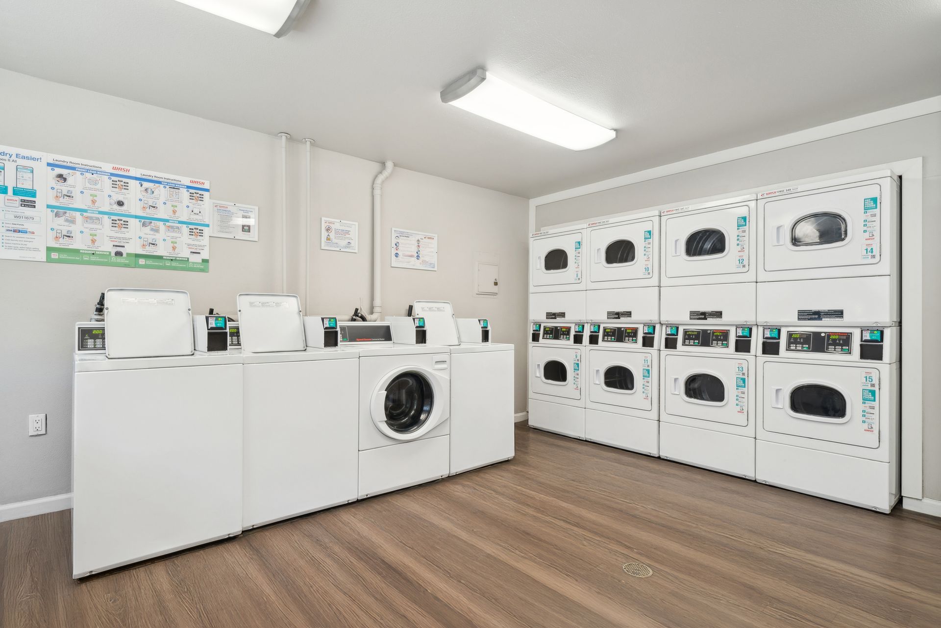 Bright laundry room with washers, dryers, folding tables, and wood flooring
