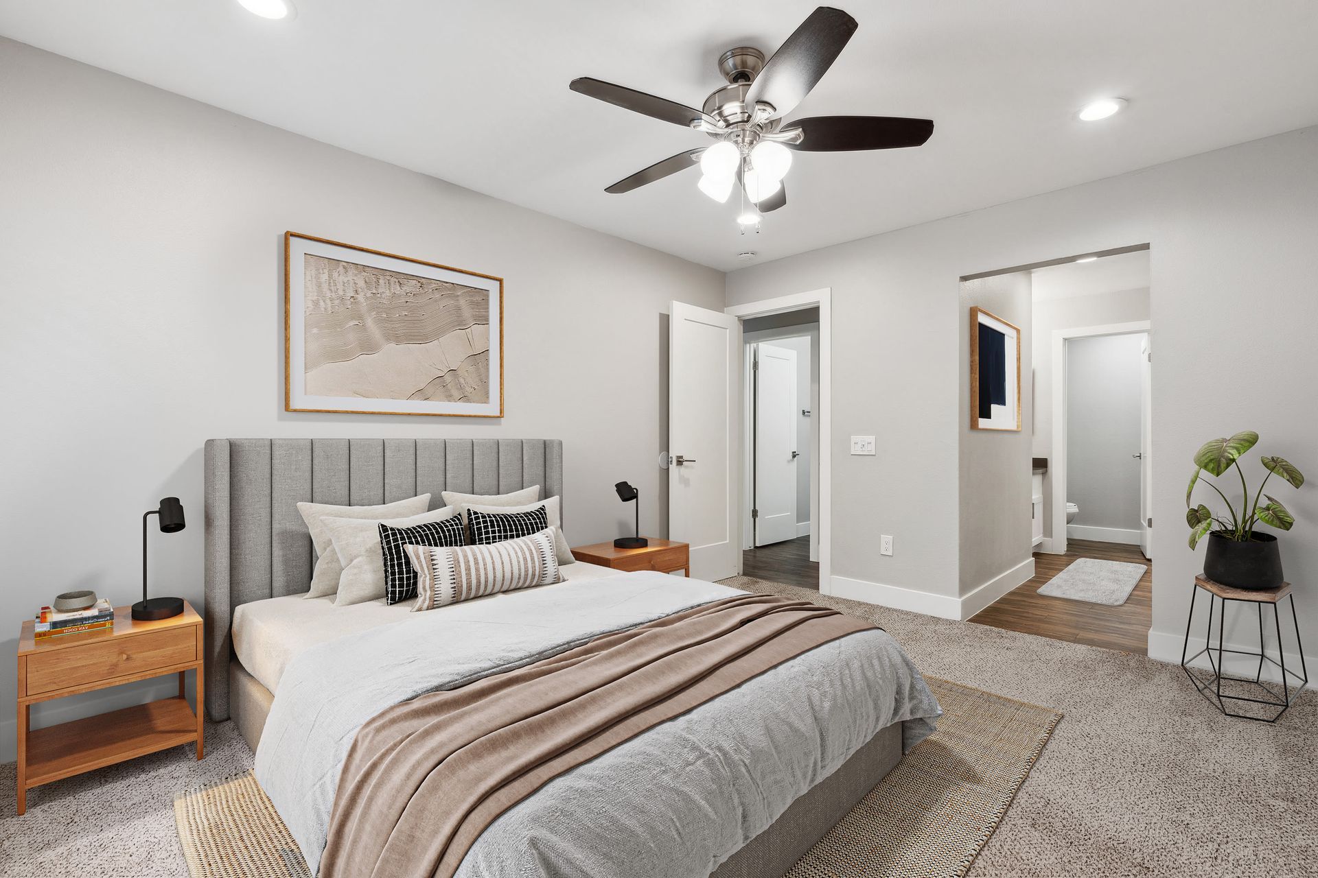 Bedroom with gray upholstered headboard, two wooden nightstands, black lamps, and ceiling fan at Muirwood apartments in Martinez, CA.