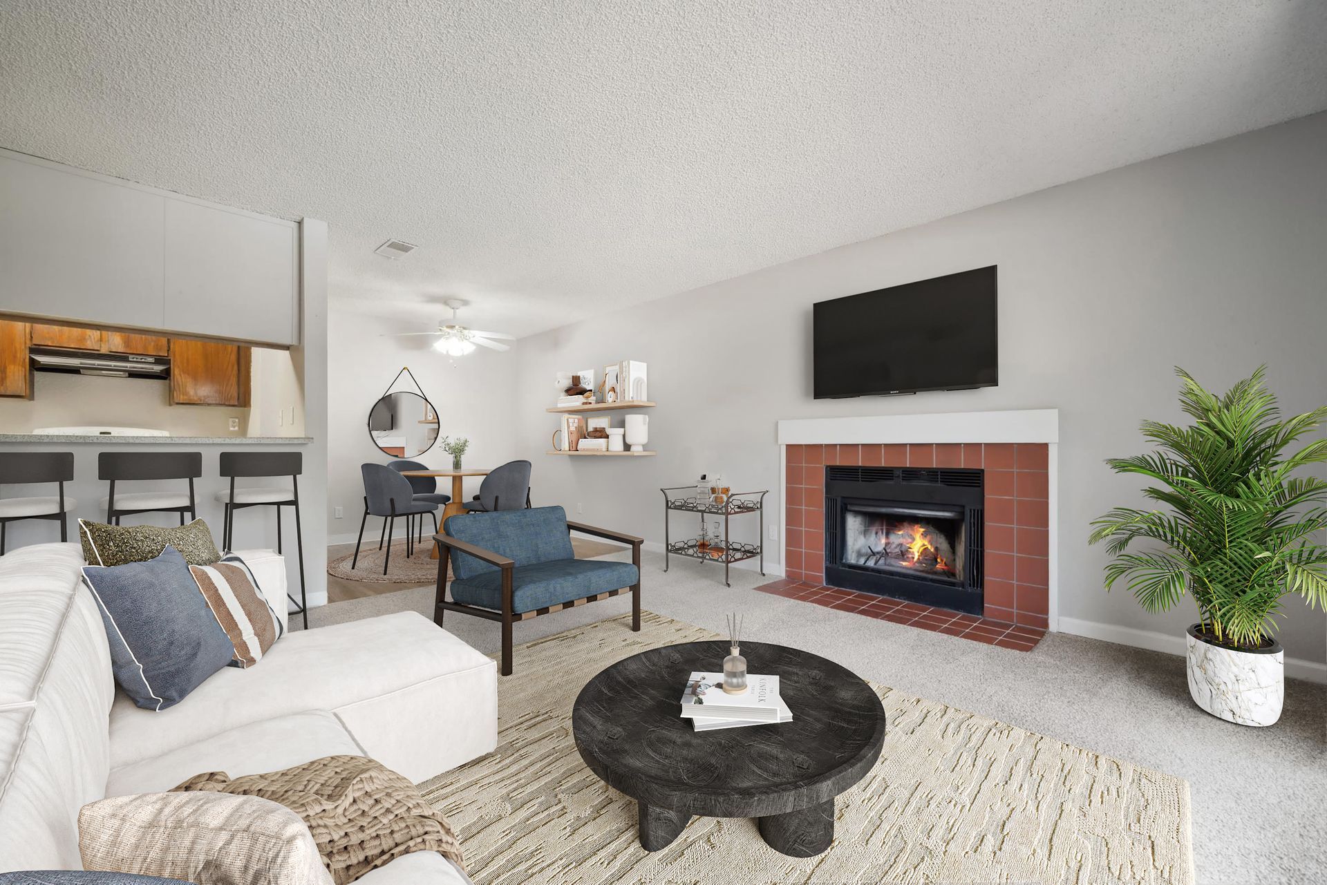 Living room with a fireplace, mounted TV, sofa and chairs, and an open kitchen with a breakfast bar at Muirwood apartments in Martinez, CA.