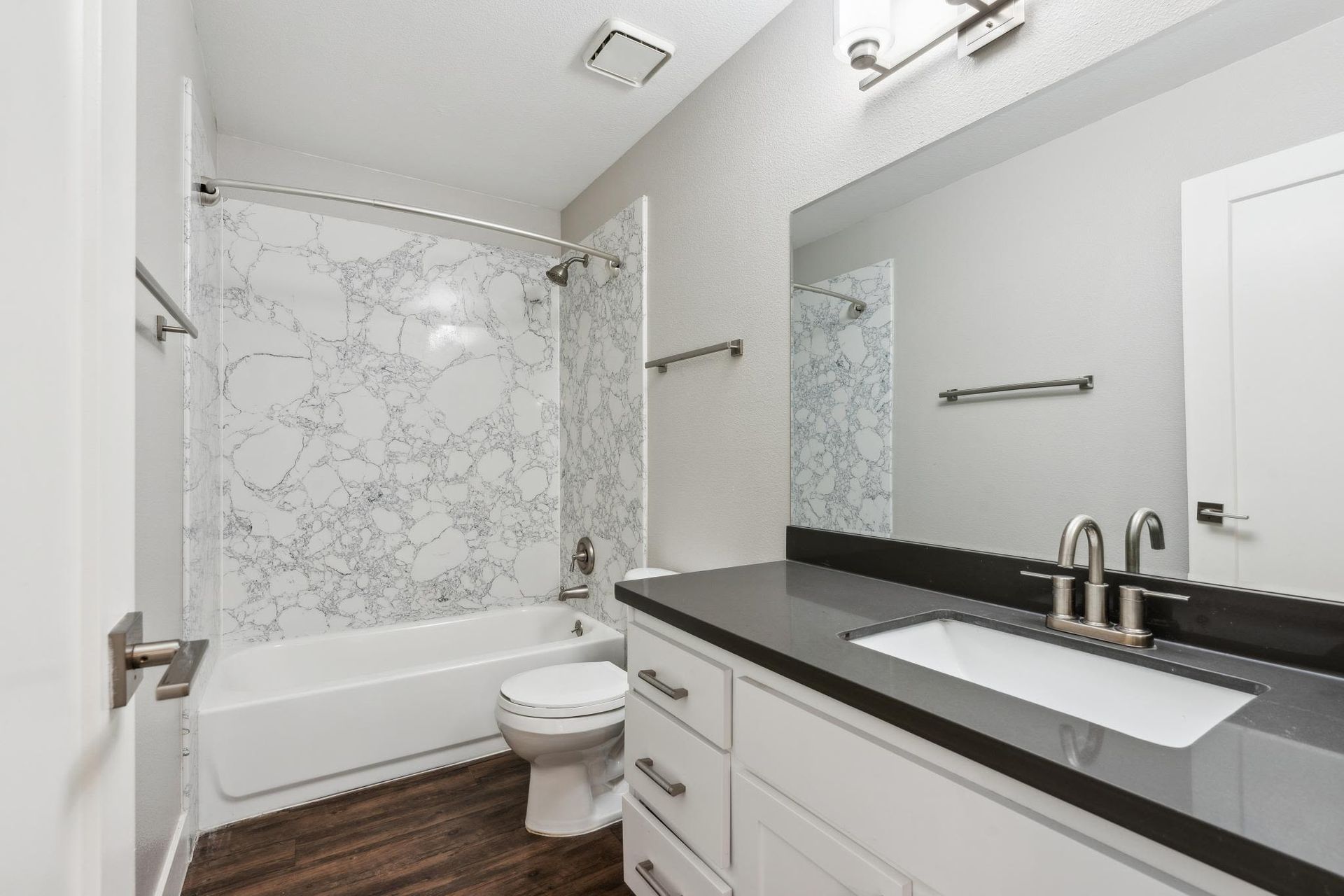 Bathroom featuring a marble-pattern shower surround, white vanity, and toilet at Muirwood apartments in Martinez, CA.