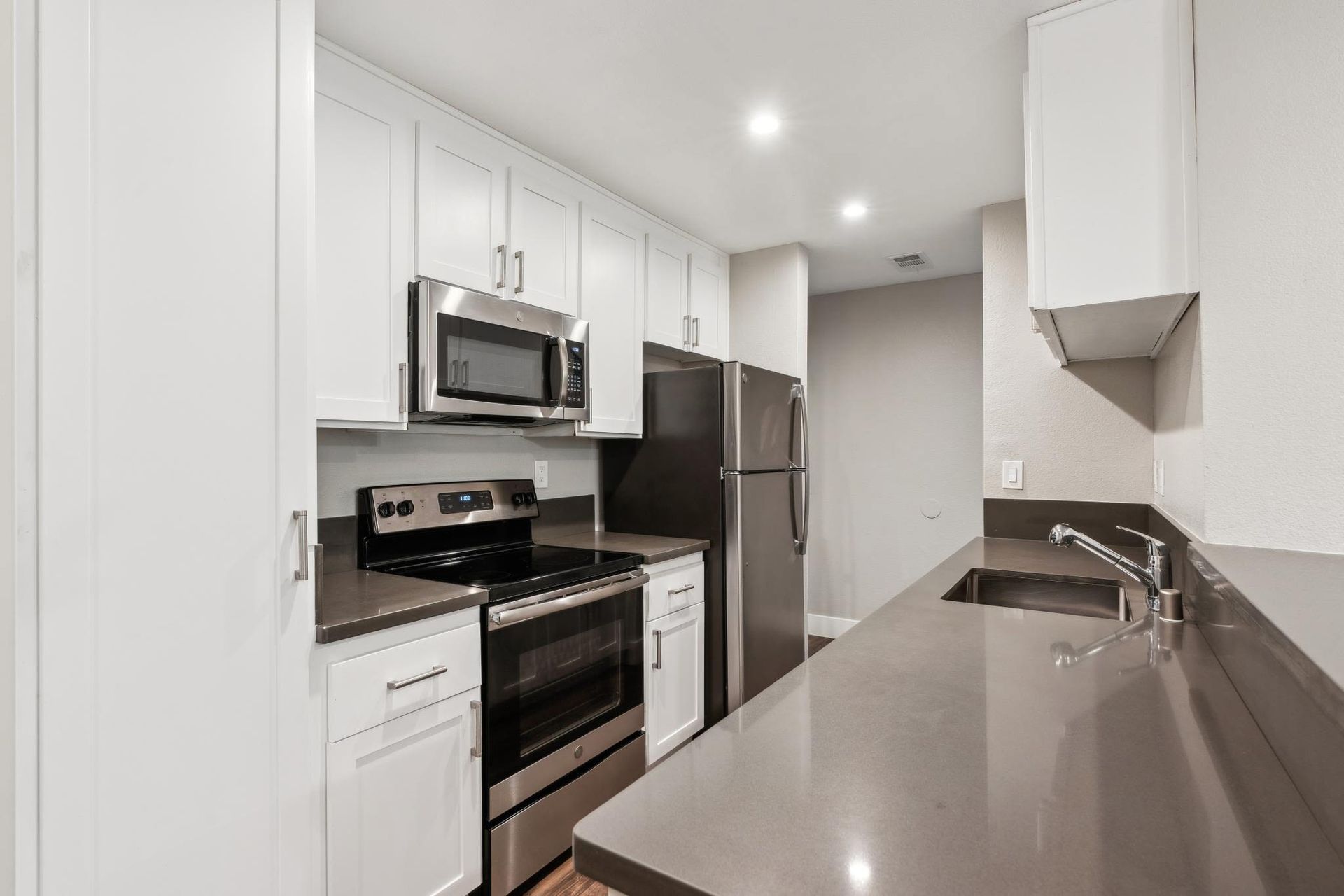 Modern white kitchen with stainless steel appliances and a long gray countertop at Muirwood apartments in Martinez, CA.