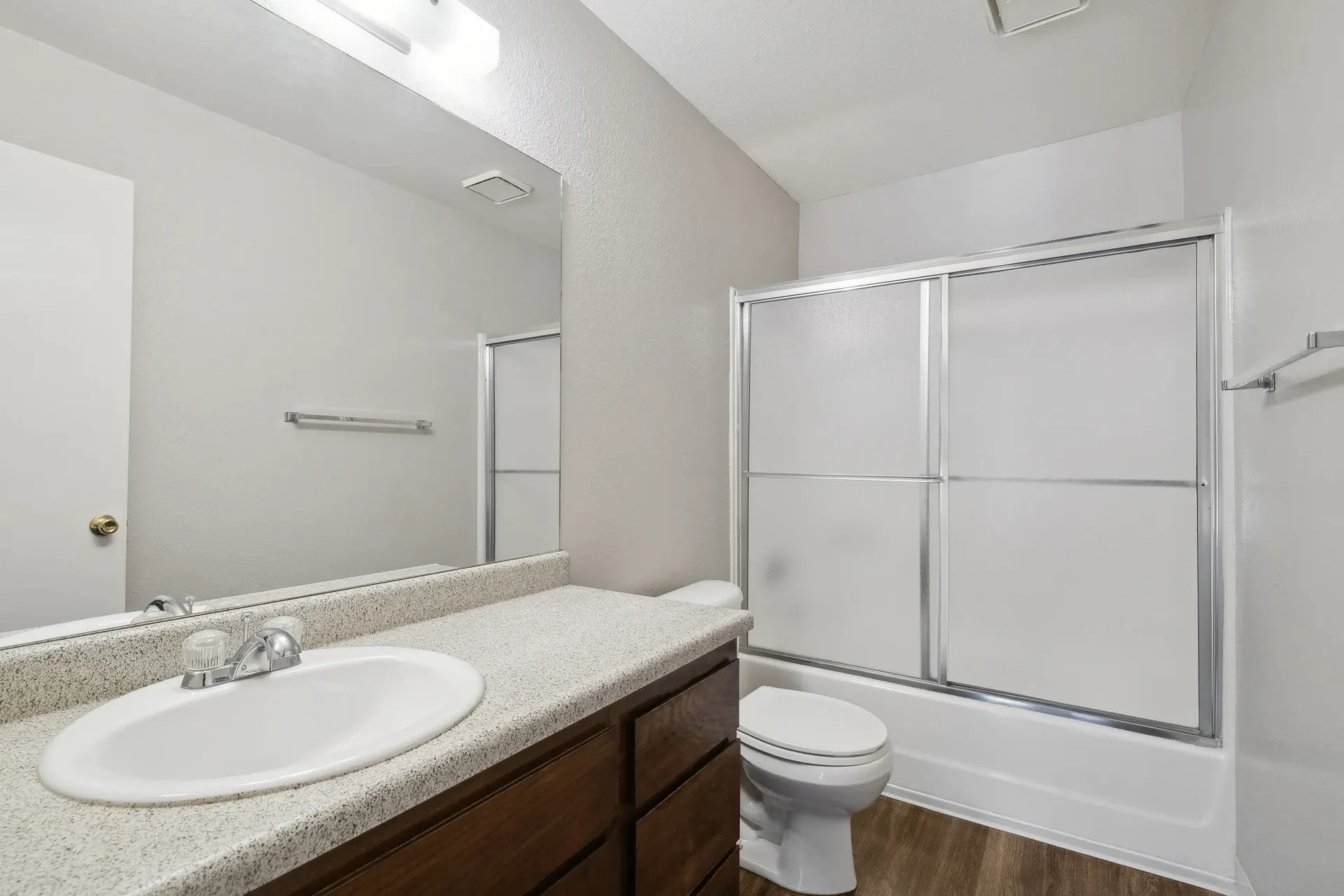 Bathroom in an apartment with a single sink vanity, mirror, toilet, and frosted glass sliding tub/shower at Muirwood apartments in Martinez, CA.