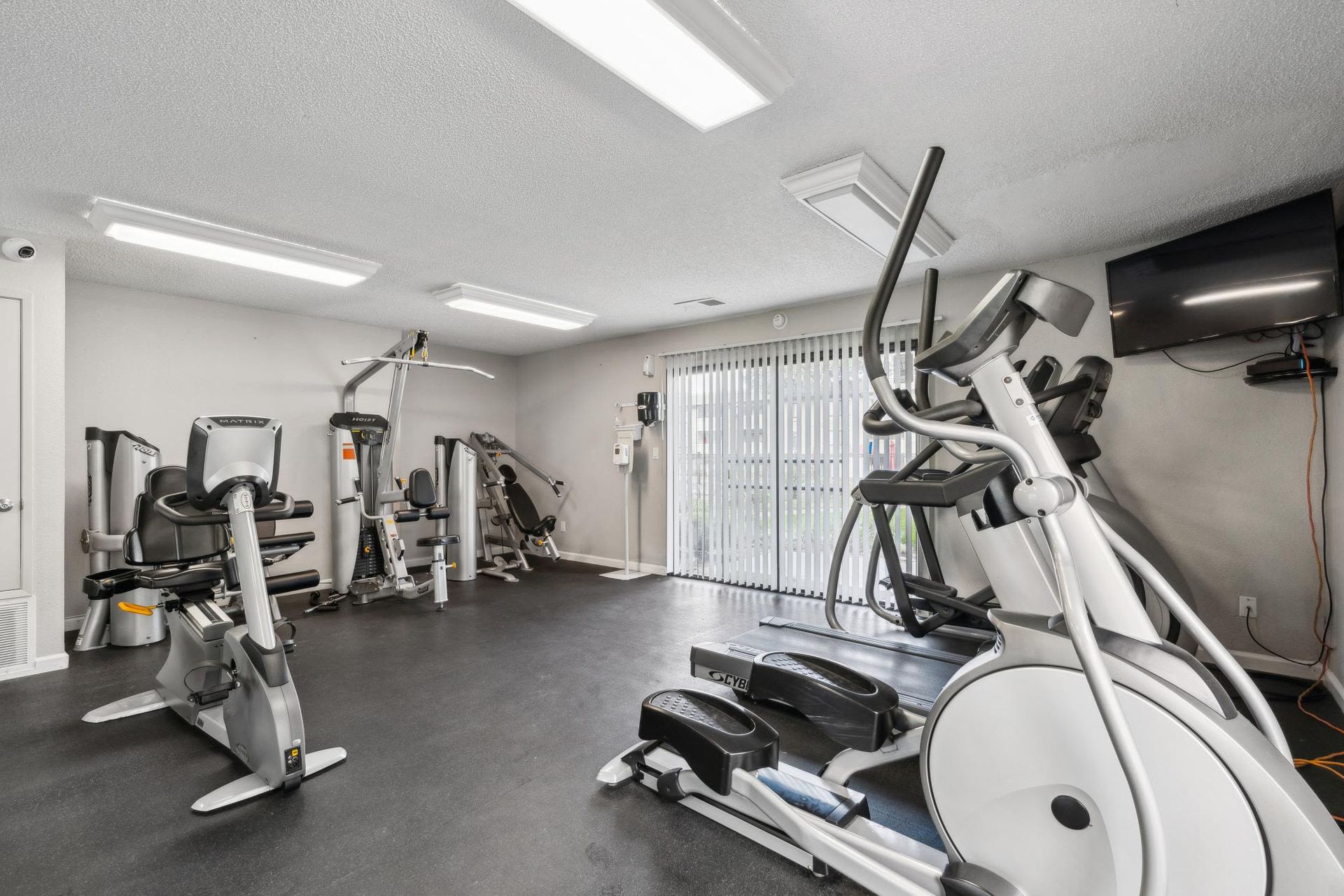 Indoor fitness center with treadmills, ellipticals, weights, and a wall-mounted TV at Muirwood apartments in Martinez, CA.