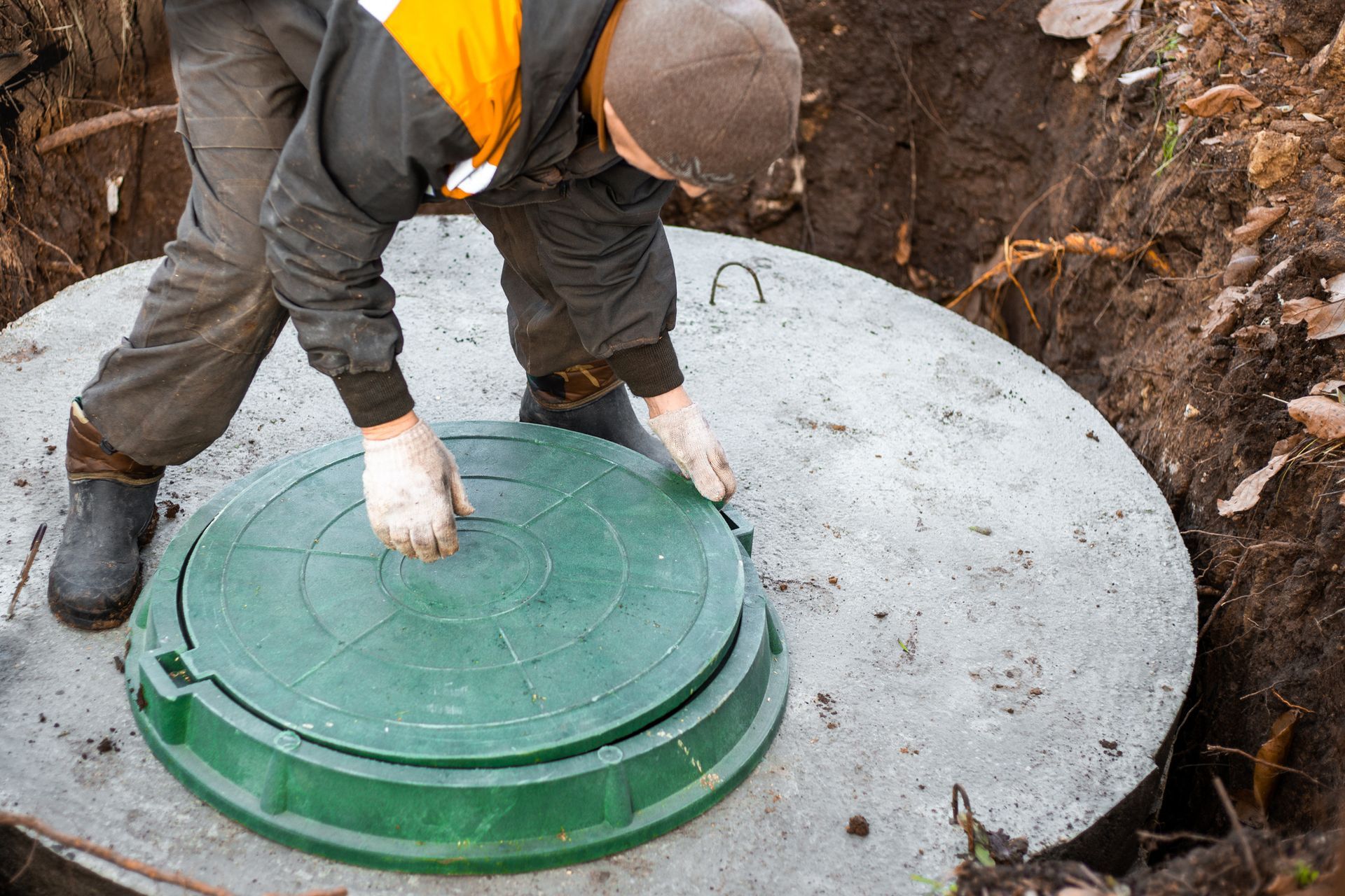 A man is opening a green manhole cover on a septic tank.