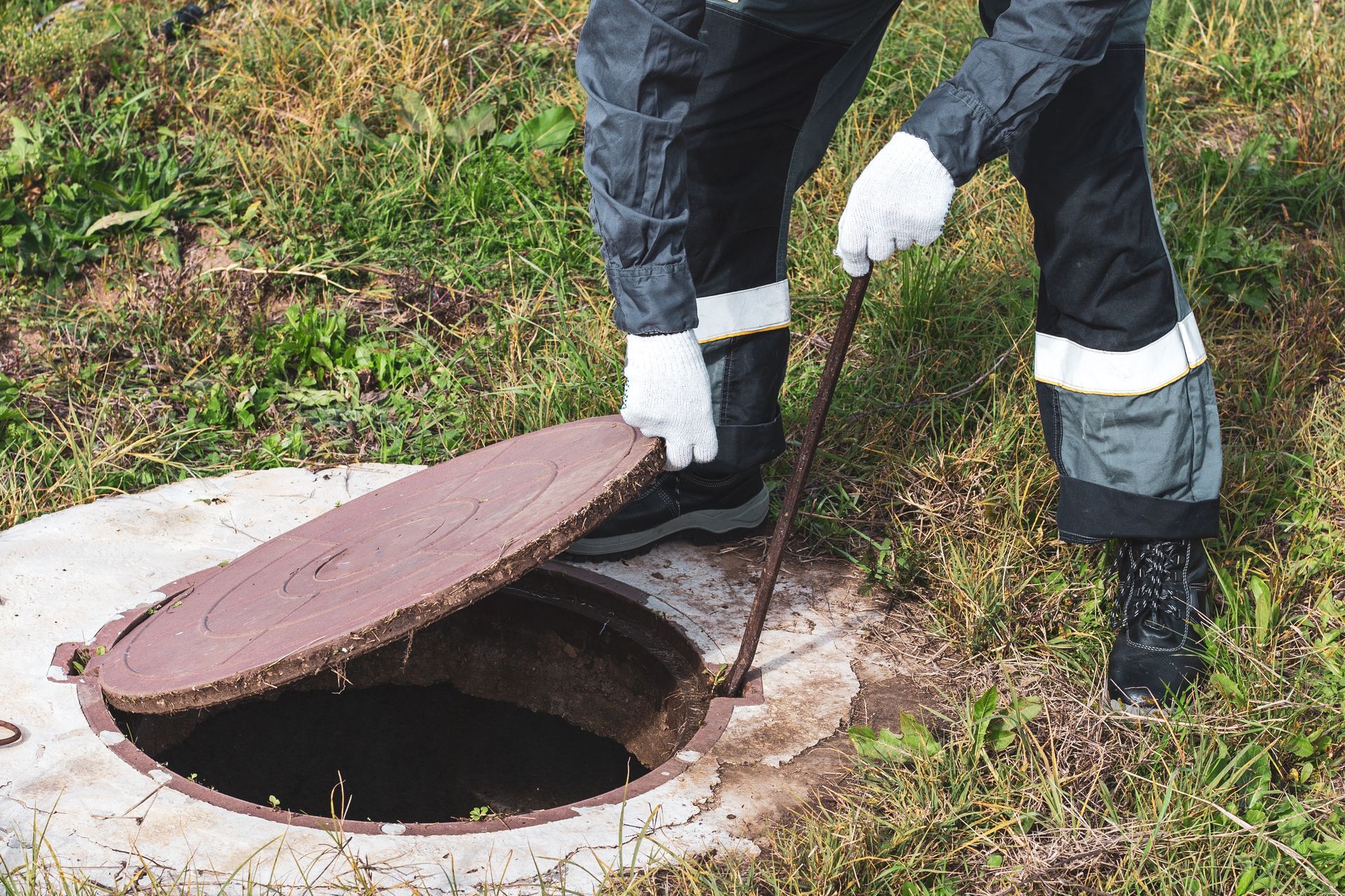 A man is opening a manhole cover with a stick.