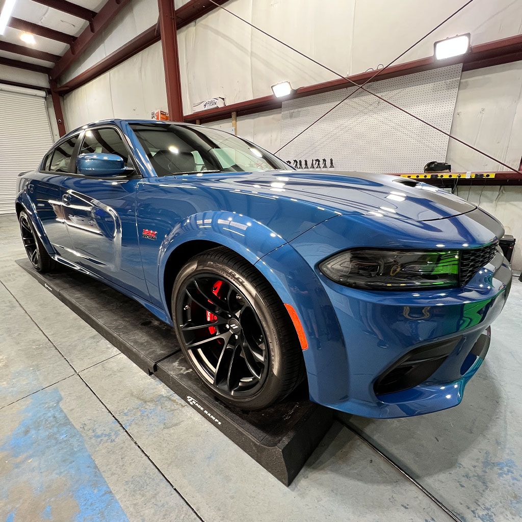 Blue Dodge Charger on a dyno in a garage, red brake calipers, black wheels.