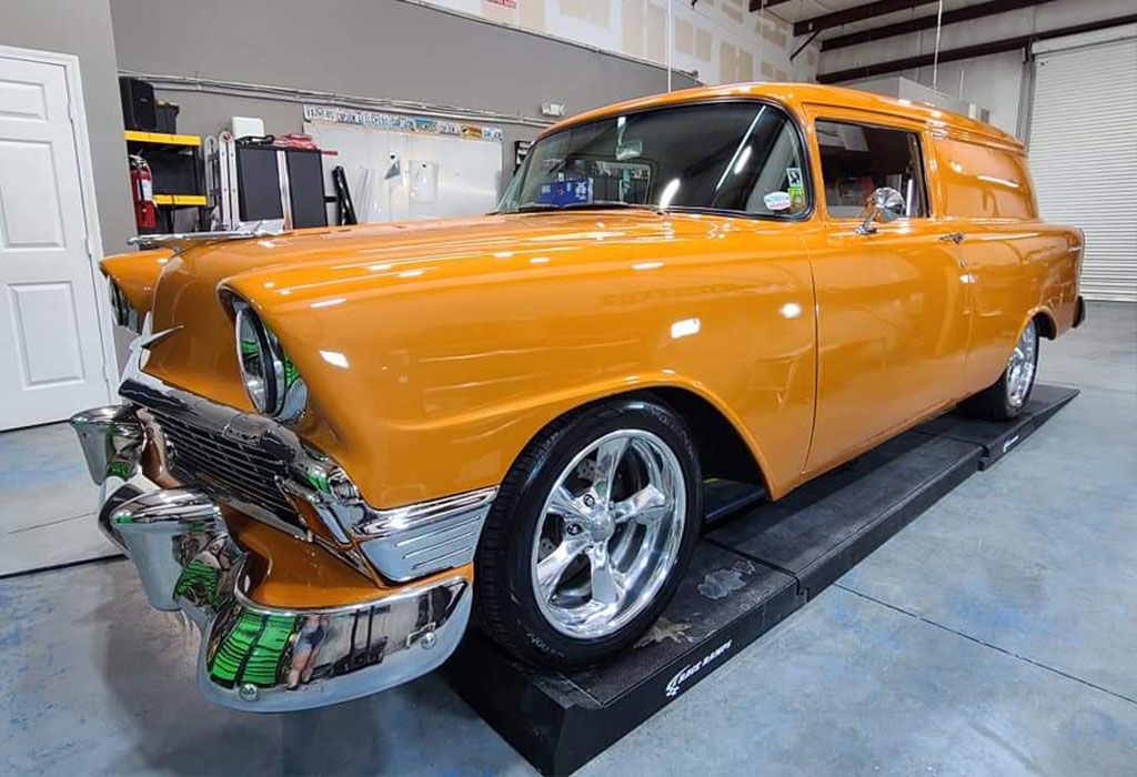 Orange classic Chevy sedan delivery. Shiny chrome, custom wheels, indoors.