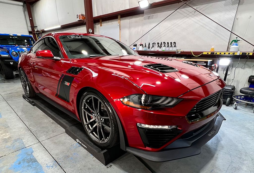 Red Ford Mustang sports car parked inside a garage, shiny paint, low angle.