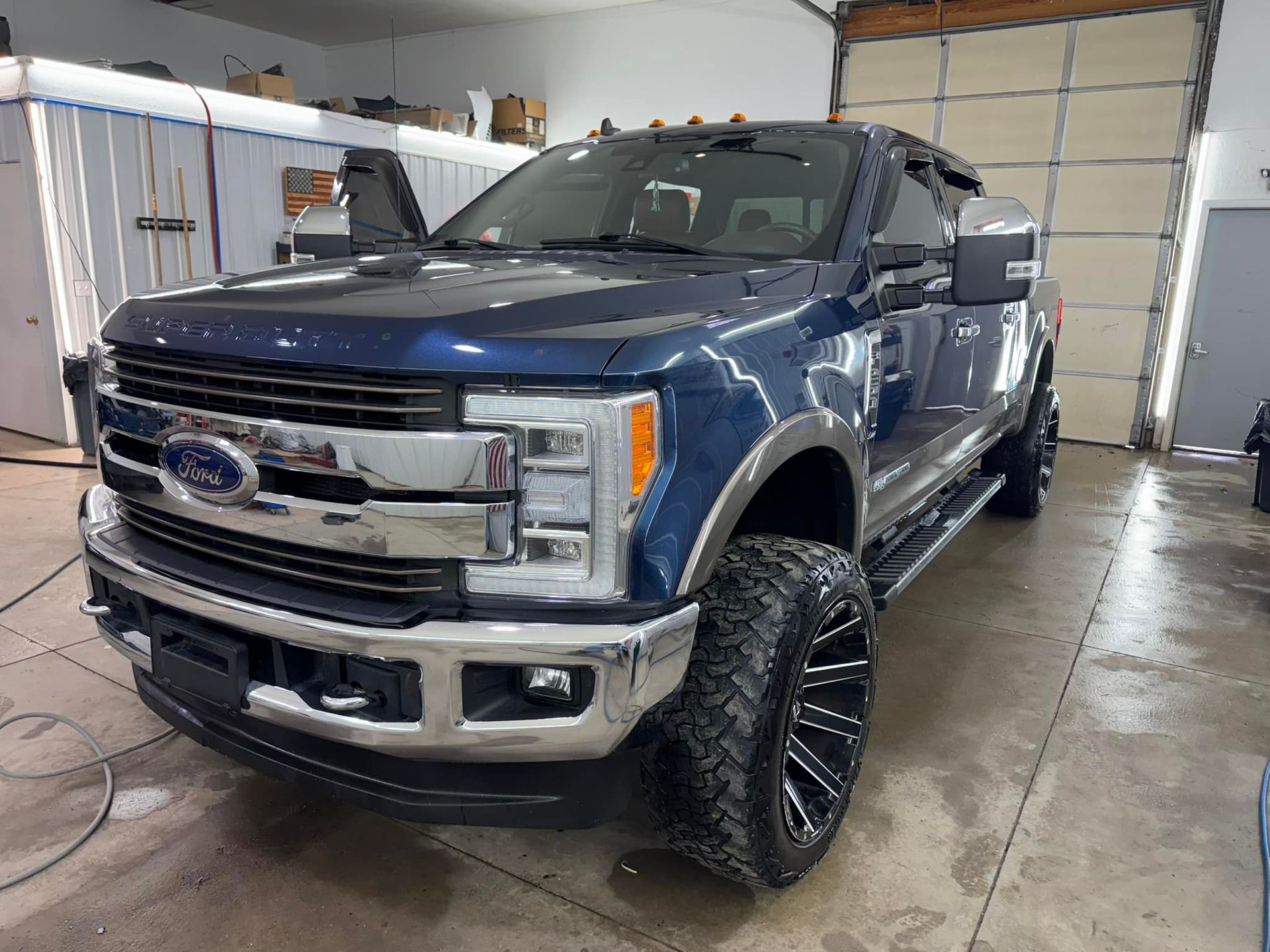 A dark blue Ford Super Duty pickup truck with aftermarket off-road tires, parked inside a garage.