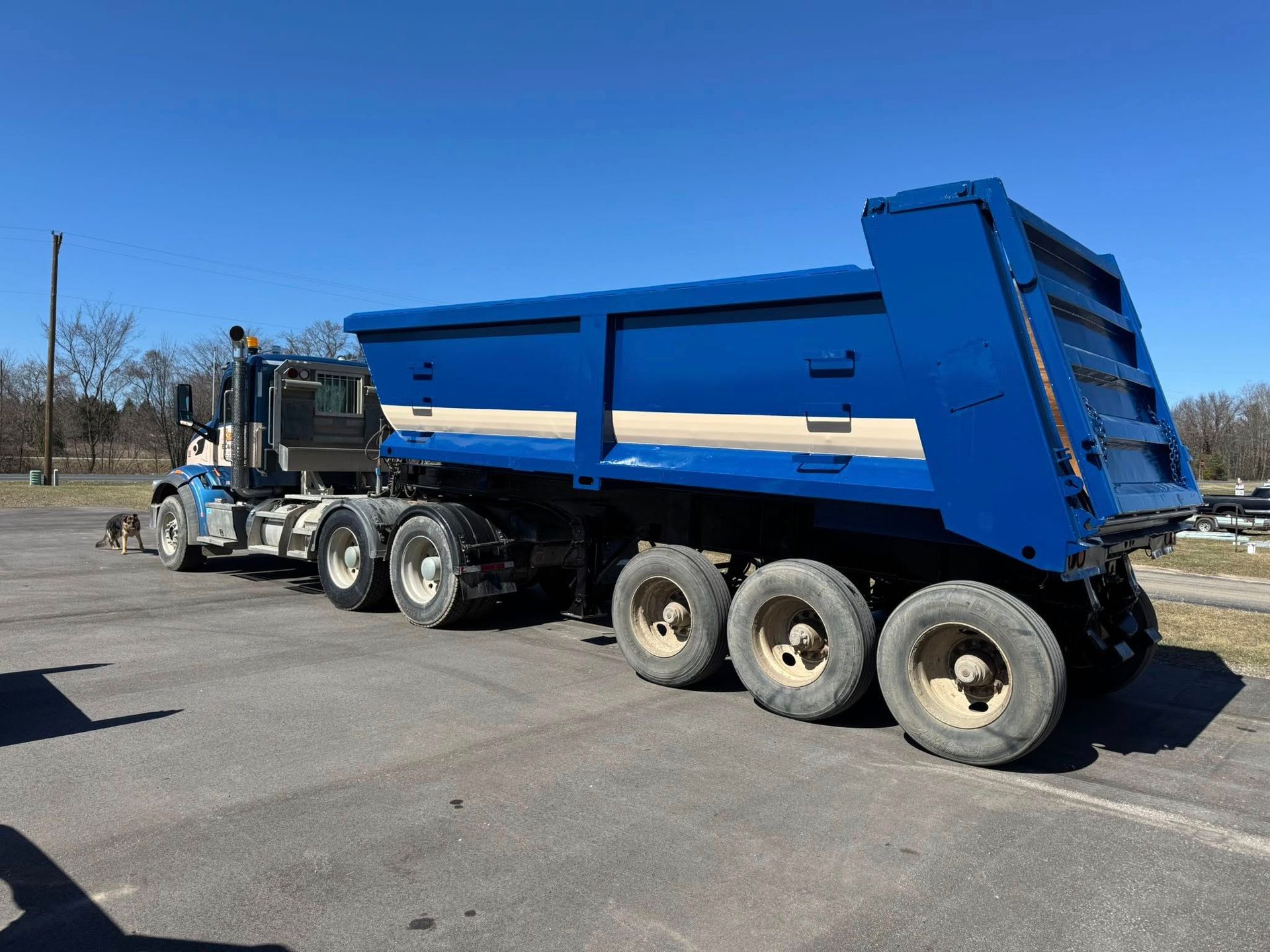 A blue dump truck sits on an asphalt lot under a clear blue sky.
