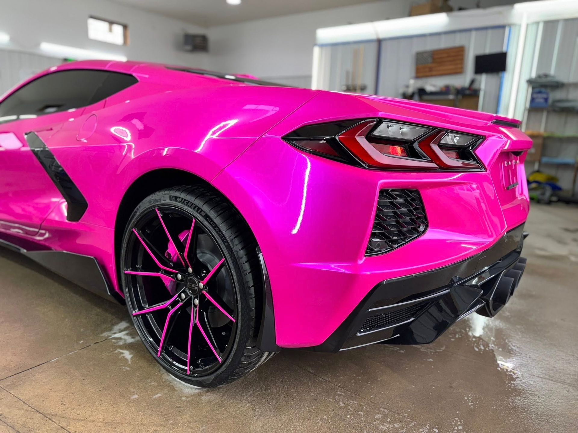 Bright pink Chevrolet Corvette parked in a garage, featuring matching pink details on the black alloy wheels.