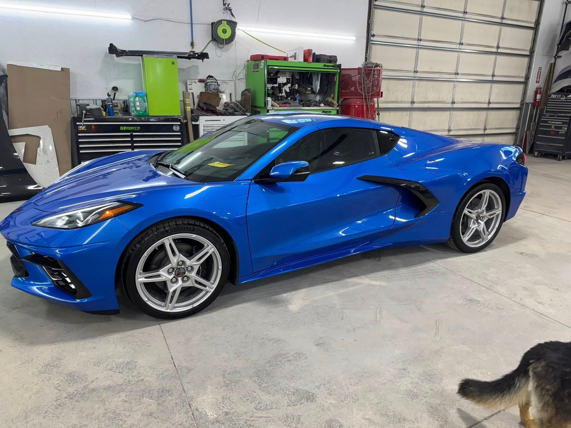 A blue Chevrolet Corvette parked inside a workshop with tools and equipment in the background.