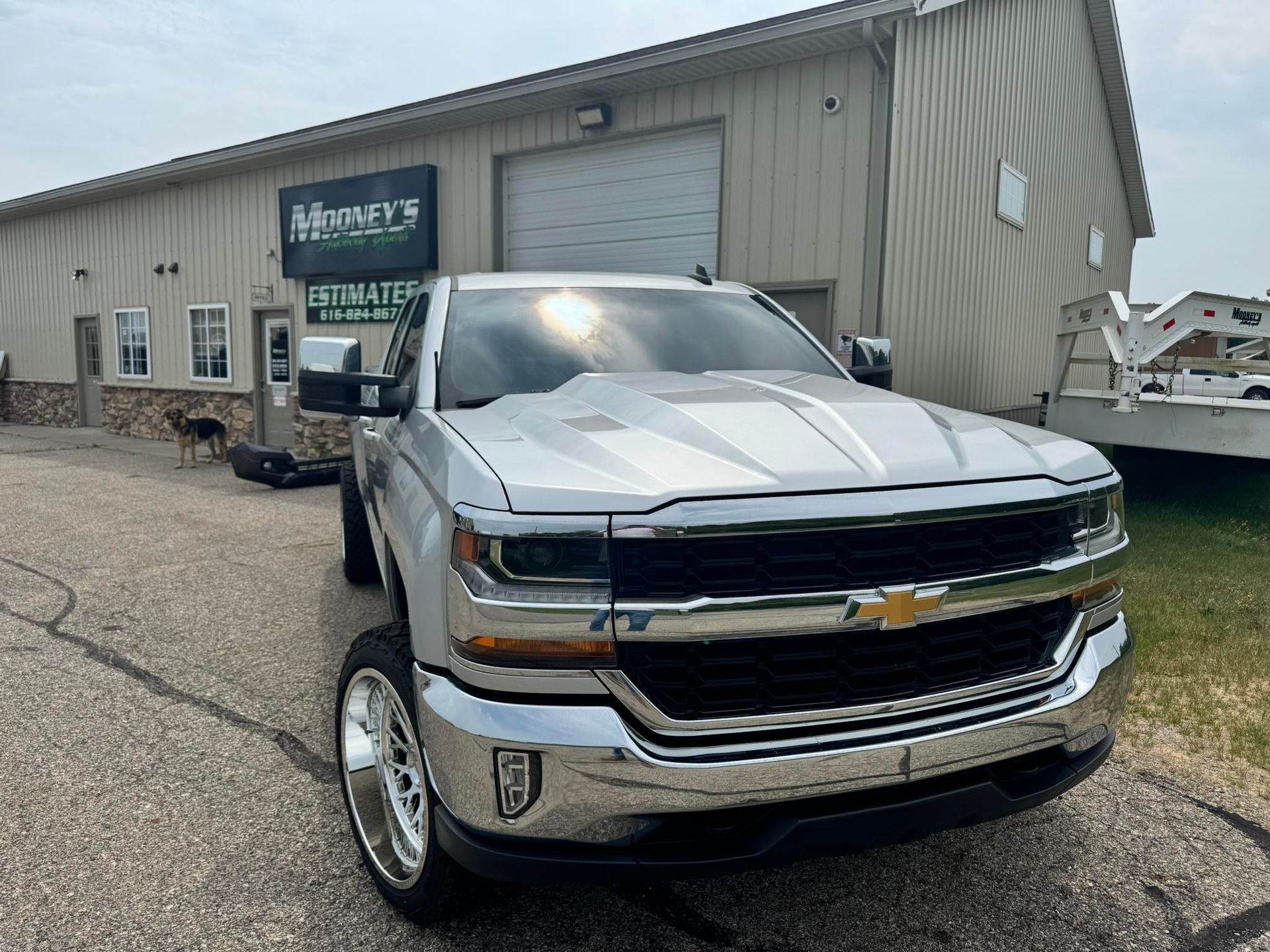 A silver lifted Chevrolet pickup truck with custom wheels parked in front of a commercial building.