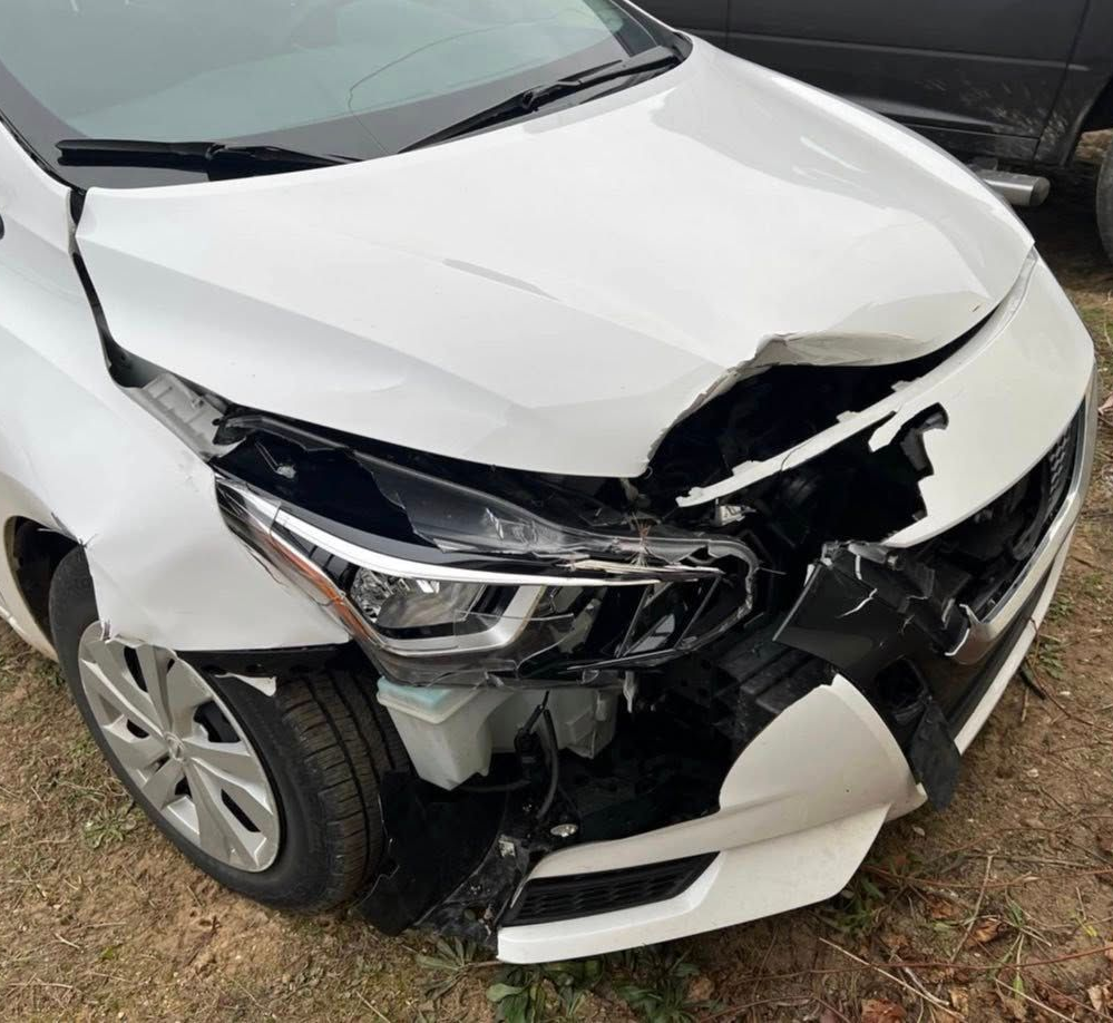 A white car with significant front-end damage, including a crumpled hood, broken bumper, and exposed internal parts.