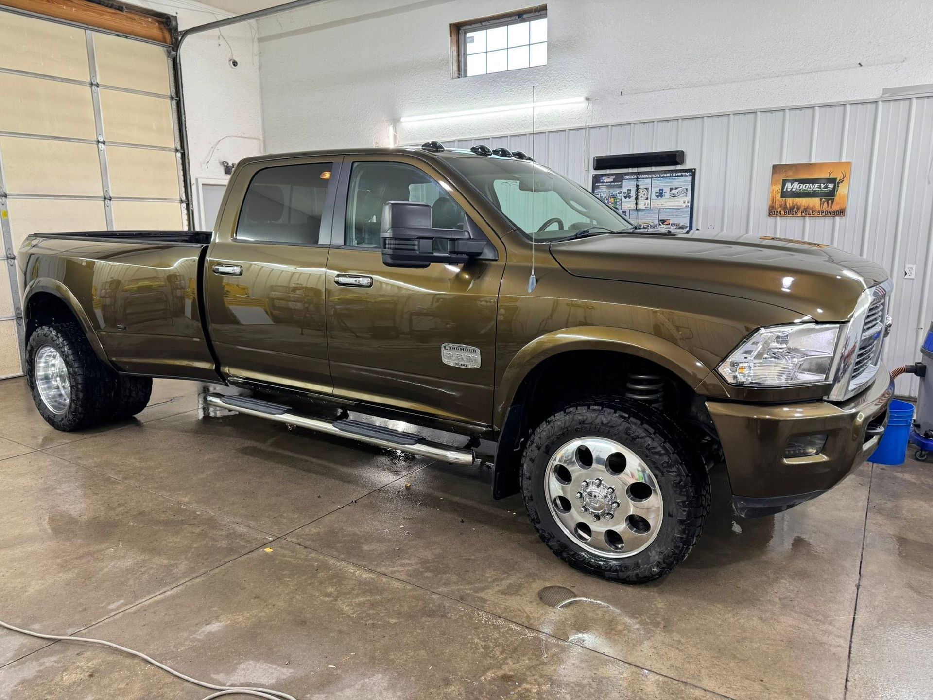 A brown Ram dually pickup truck parked in a well-lit, industrial garage.