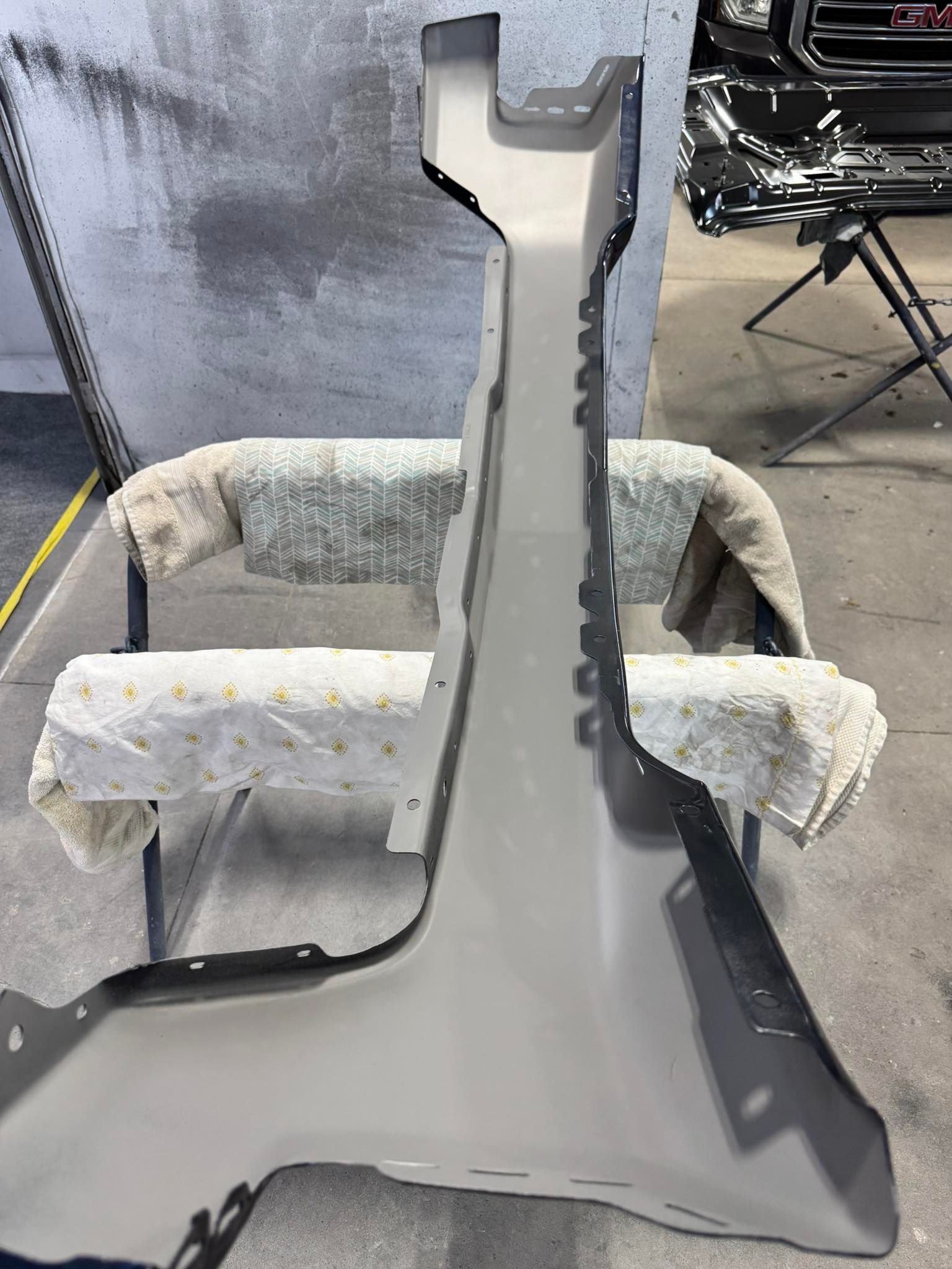 A light-colored automotive pillar reinforcement part mounted on a stand in a workshop.
