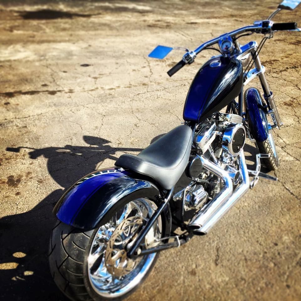 A blue and black custom motorcycle parked on a paved surface, viewed from a high angle behind the seat.