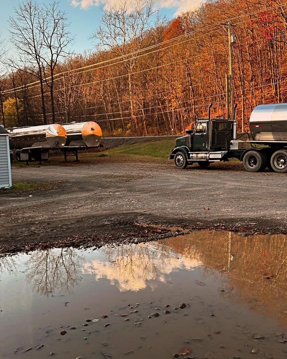 Autumn farmyard with a tanker truck, storage tanks, and a muddy puddle reflecting trees and sky Autumn farmyard with a tanker truck, storage tanks, and a muddy puddle reflecting trees and sky