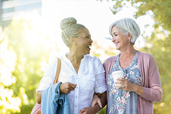 two older women are walking down a sidewalk and talking to each other .