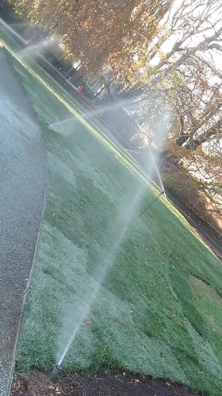 Lawn sprinkler spraying water in front of a tan building under a clear sky