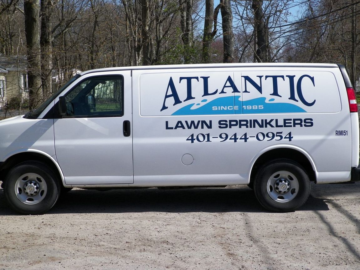 Sprinklers watering a green lawn in front of a house with shrubs and flowerbeds.