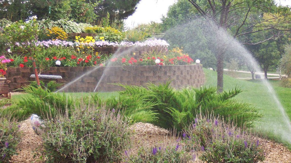 Lawn sprinkler spraying water in front of a tan building under a clear sky