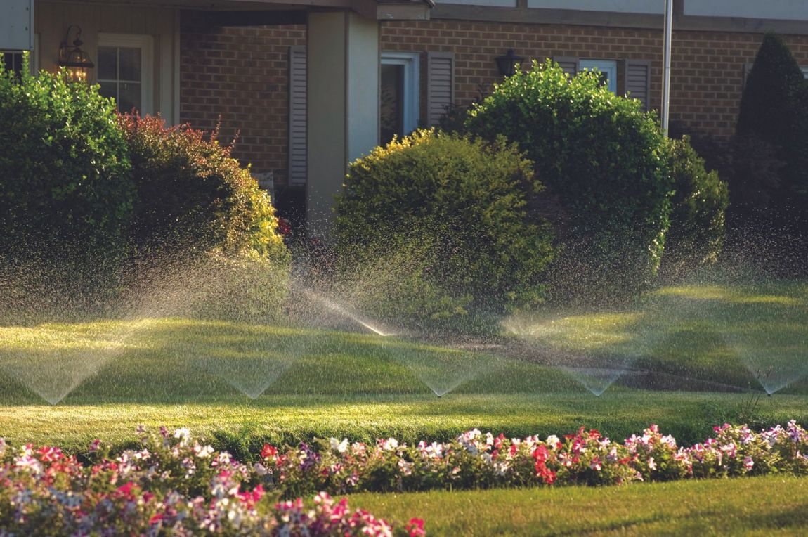 Lawn sprinkler spraying water before a tan building on a sunny day