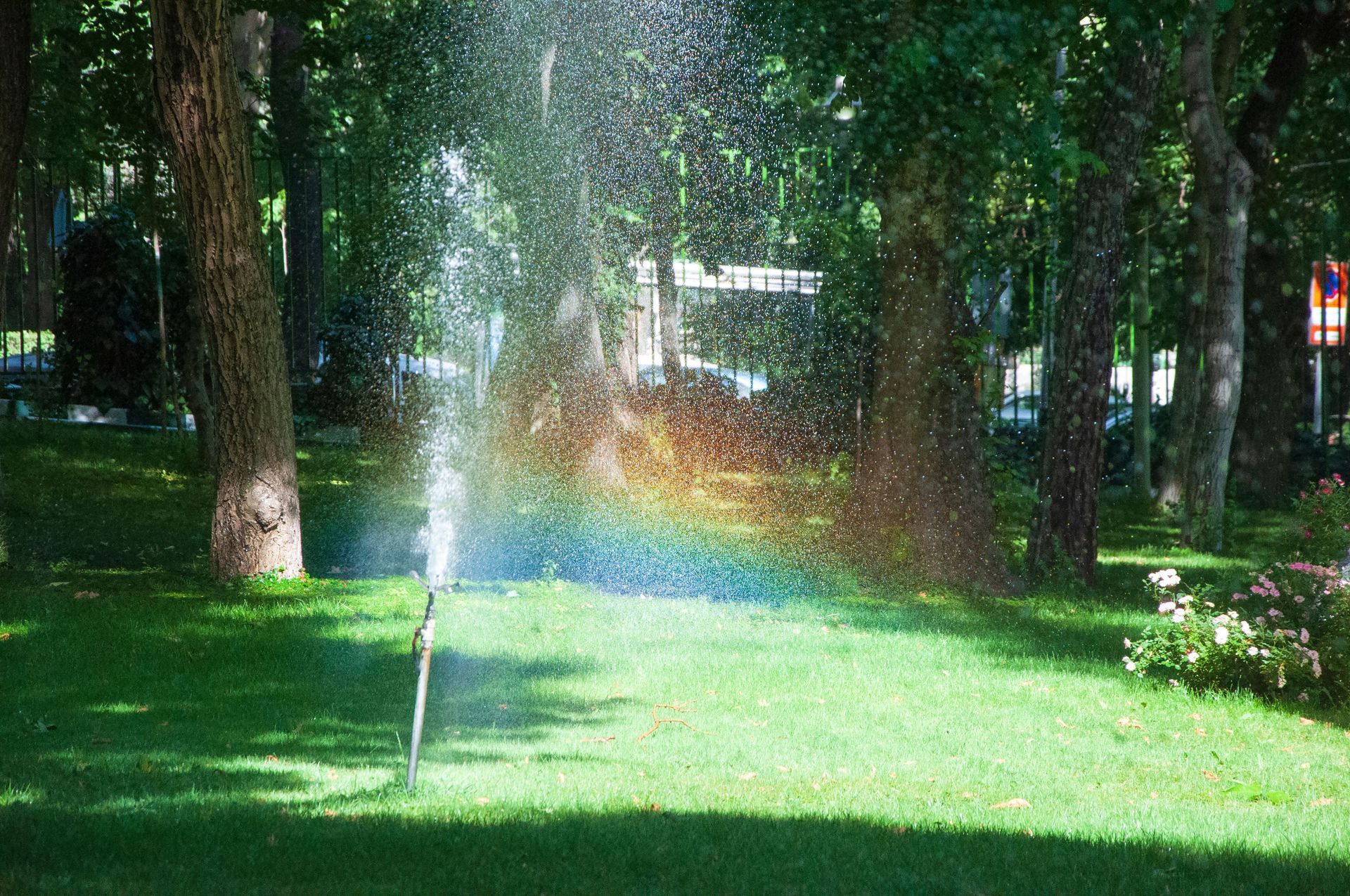 Lawn sprinkler spraying water in front of a tan building under a clear sky