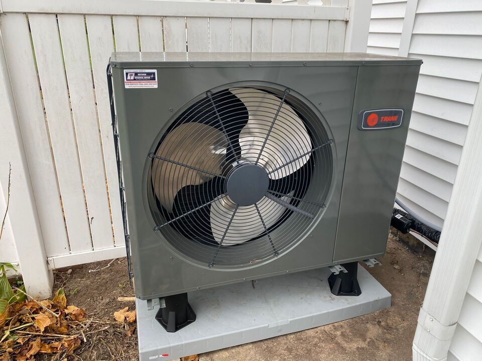 A large fan is sitting outside of a house next to a white fence.