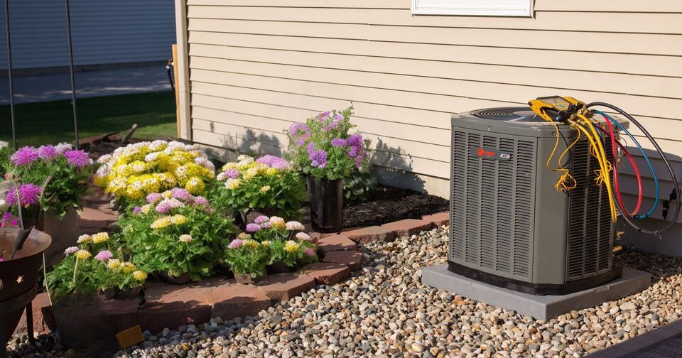 An air conditioner is sitting in a garden next to a house.
