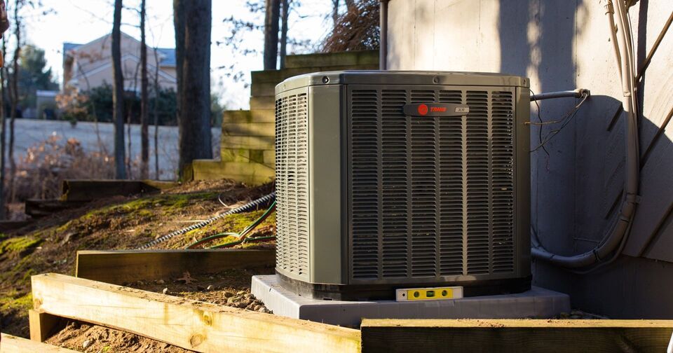 An air conditioner is sitting on the side of a building next to a wooden fence.