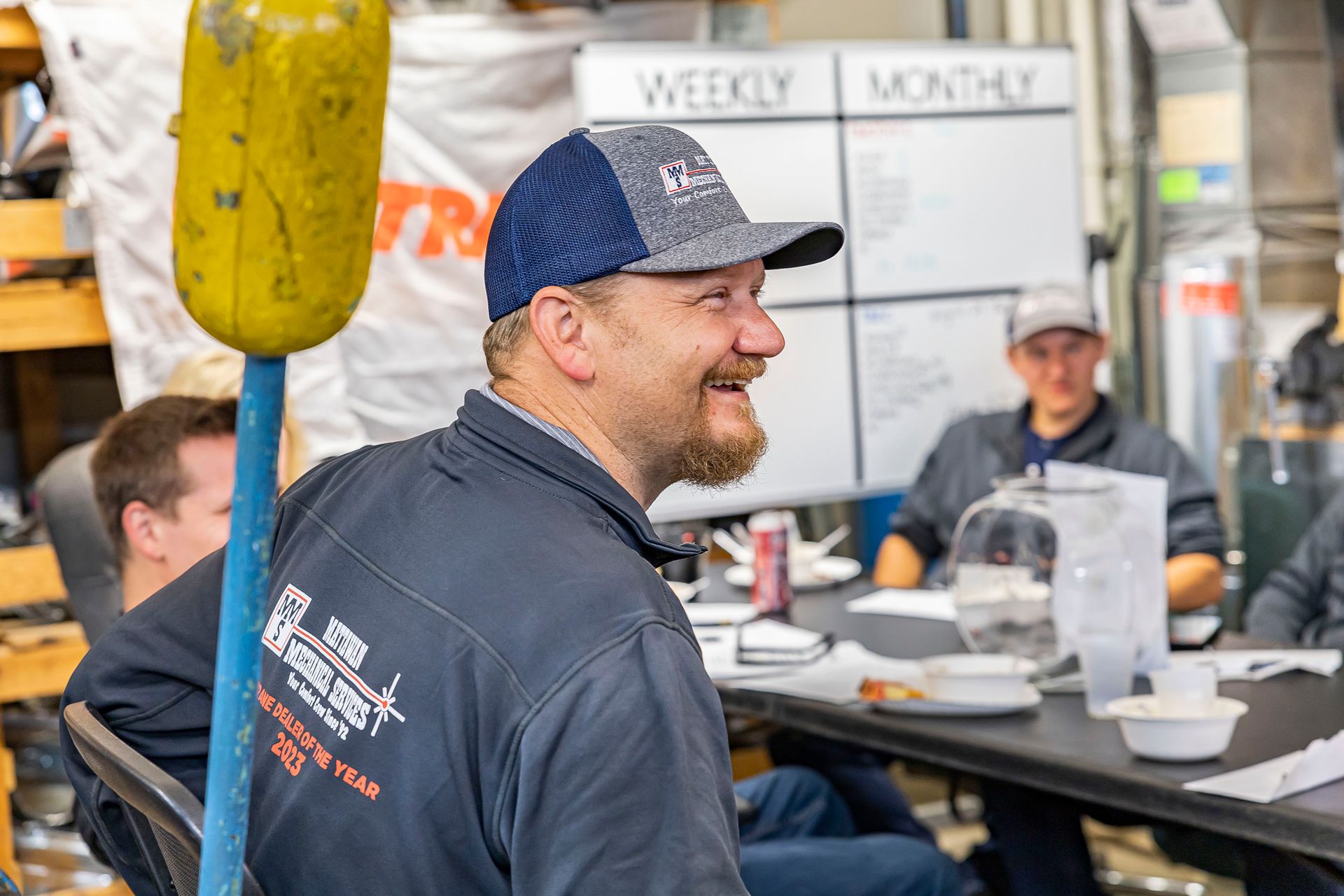 A man sitting at a table with a weekly and monthly board behind him